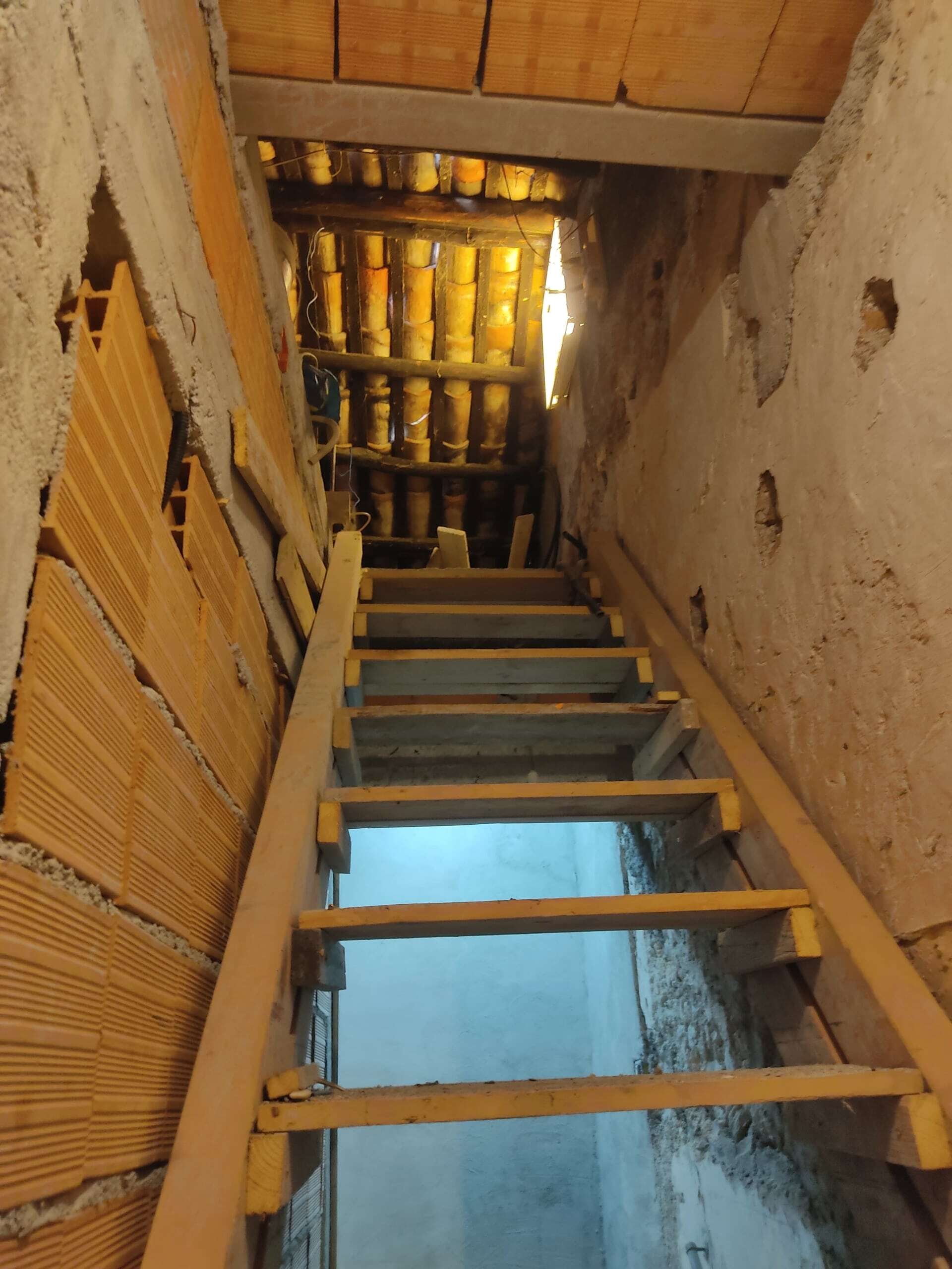 Impalcatura in fase di ristrutturazione di un locale sottostante al tetto in costruzione, con travi e isolamento isolante visibile, ambiente di cantiere con elementi in legno e muri in mattoni.