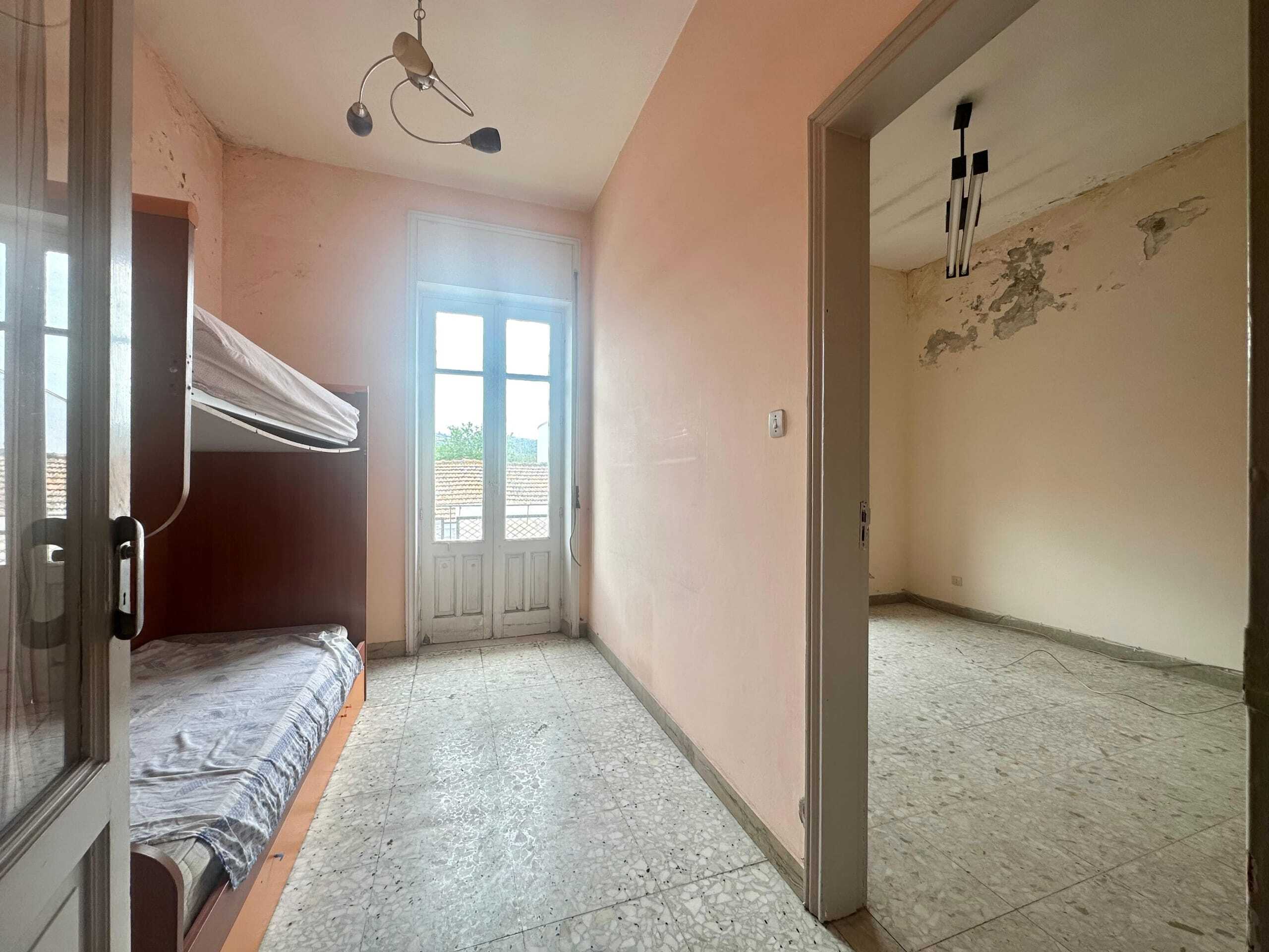 Auricolto interno di un appartamento in fase di ristrutturazione, con pareti color pesca, pavimento in terrazzo chiaro e grandi finestre che illuminano la stanza.