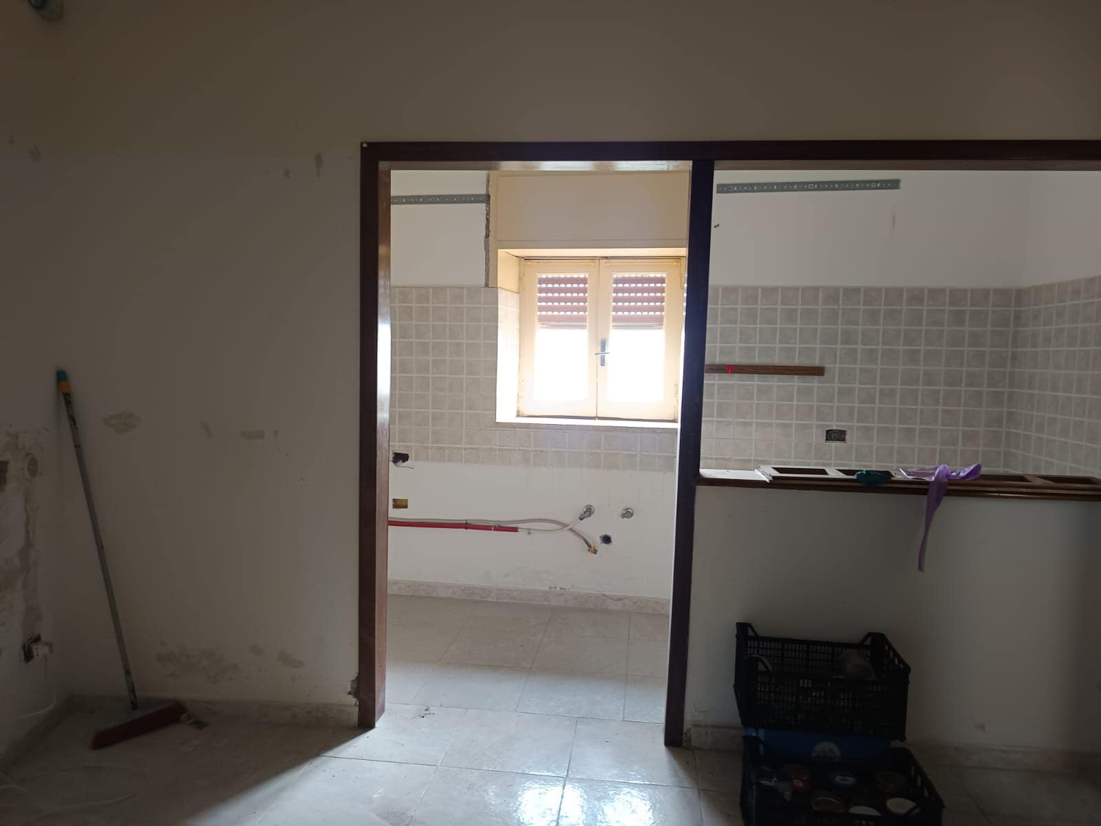 Finestra luminosa in cucina in fase di ristrutturazione, con pareti in piastrelle beige, spazi vuoti per mobili e lavori in corso, perfetta per ambienti moderni e funzionali.