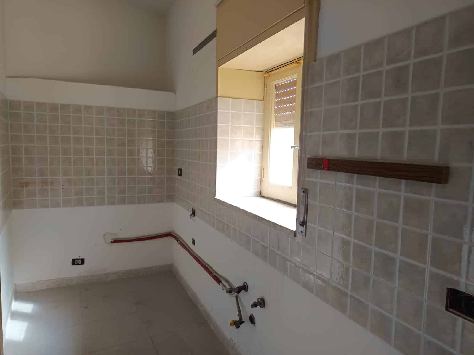 Immagine di una cucina in fase di ristrutturazione con pareti rivestite di piastrelle beige e una finestra che permette l'ingresso di luce naturale. I lavori di installazione e rifinitura sono ancora in corso.