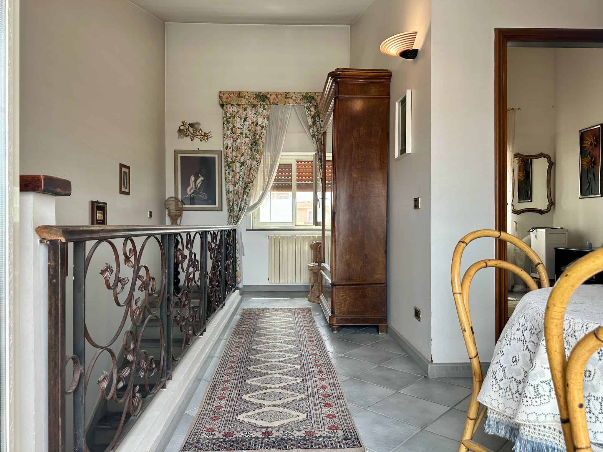 Ingresso di casa con ringhiera in ferro battuto, arredamento classico, tappeto orientale, finestra luminosa e decorazioni vintage.
