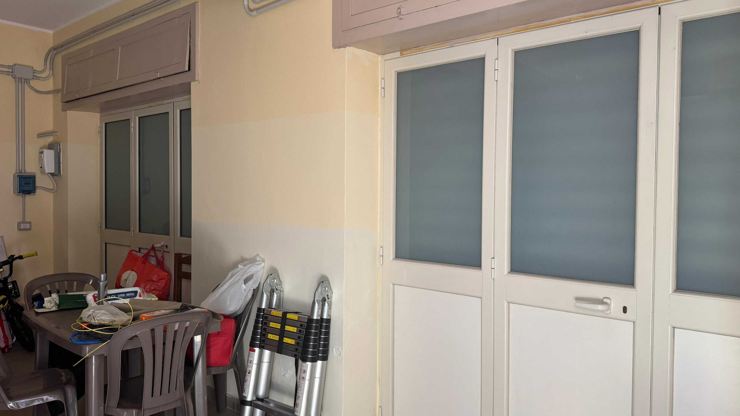 Finestra e porta scorrevole in PVC con vetri opachi in un ambiente abitativo, ideale per soluzioni di isolamento e sicurezza, con arredi e strumenti di manutenzione visibili.