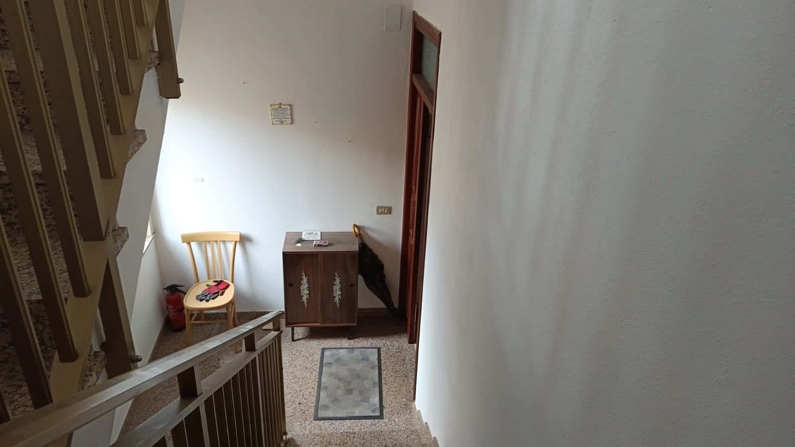 Scaletta interna di un appartamento con corrimano in legno, anche un'area di ingresso con piccola consolle e alcuni oggetti, ambientazione domestica ordinata e luminosa.
