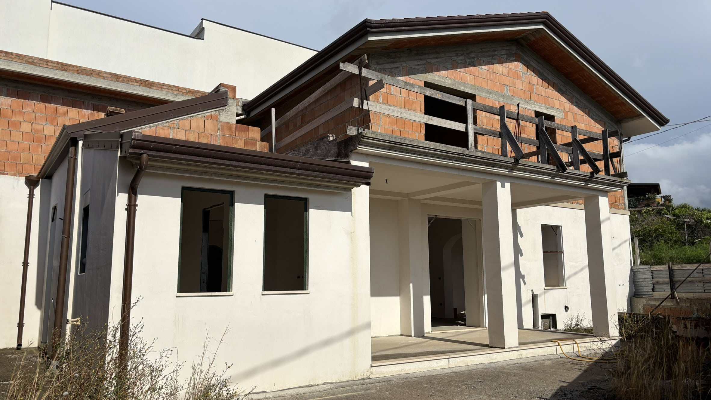 1 Nuova casa in costruzione con pareti bianche, finestre grandi e balcone in legno, in fase di completamento e ristrutturazione.