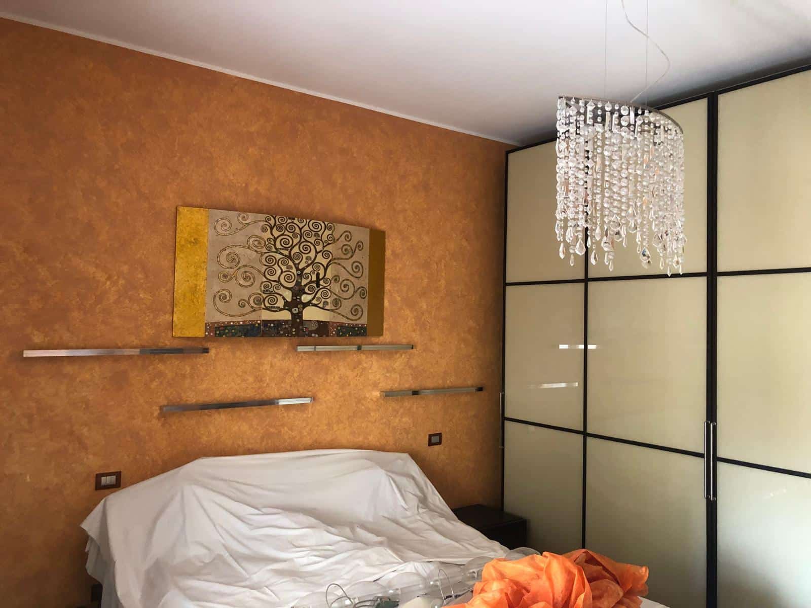 Elegante camera da letto con pareti color terracotta, grande armadio a scorrevole e lampadario in cristallo, stile moderno e confortevole, ideale per case e appartamenti di valore.