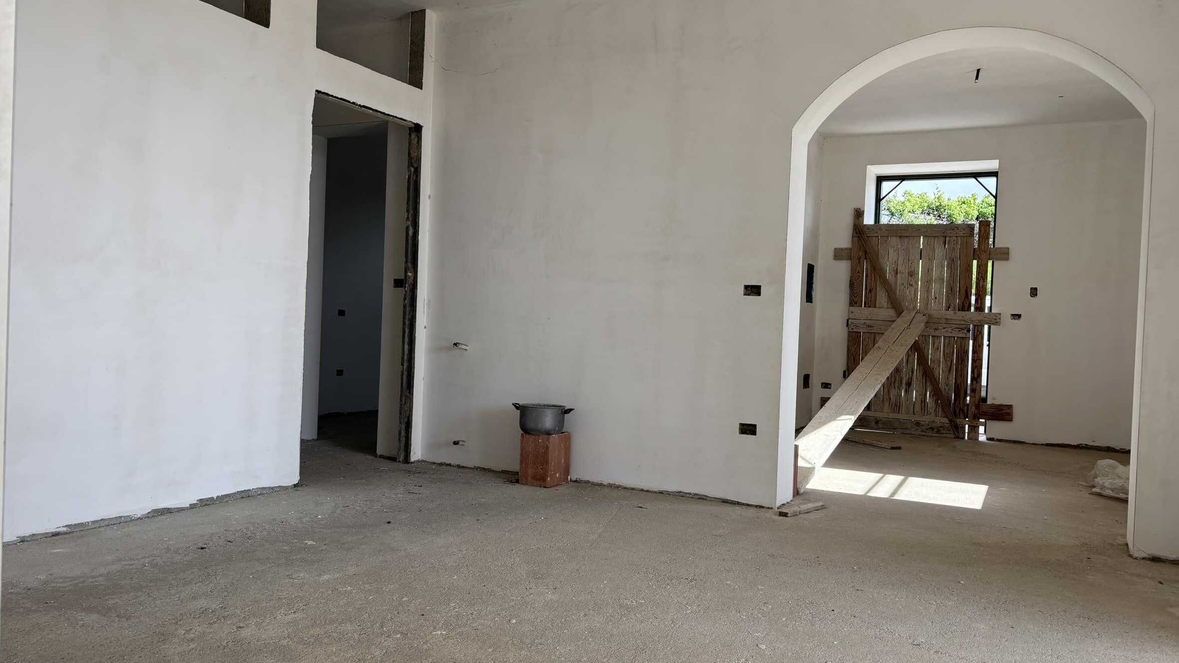 Faro casa in costruzione con pareti dipinte di bianco e dettagli in legno, ambiente interno in fase di finitura, spazio luminoso e aperto con finestre e porta temporanea, pronto per essere personalizzato.