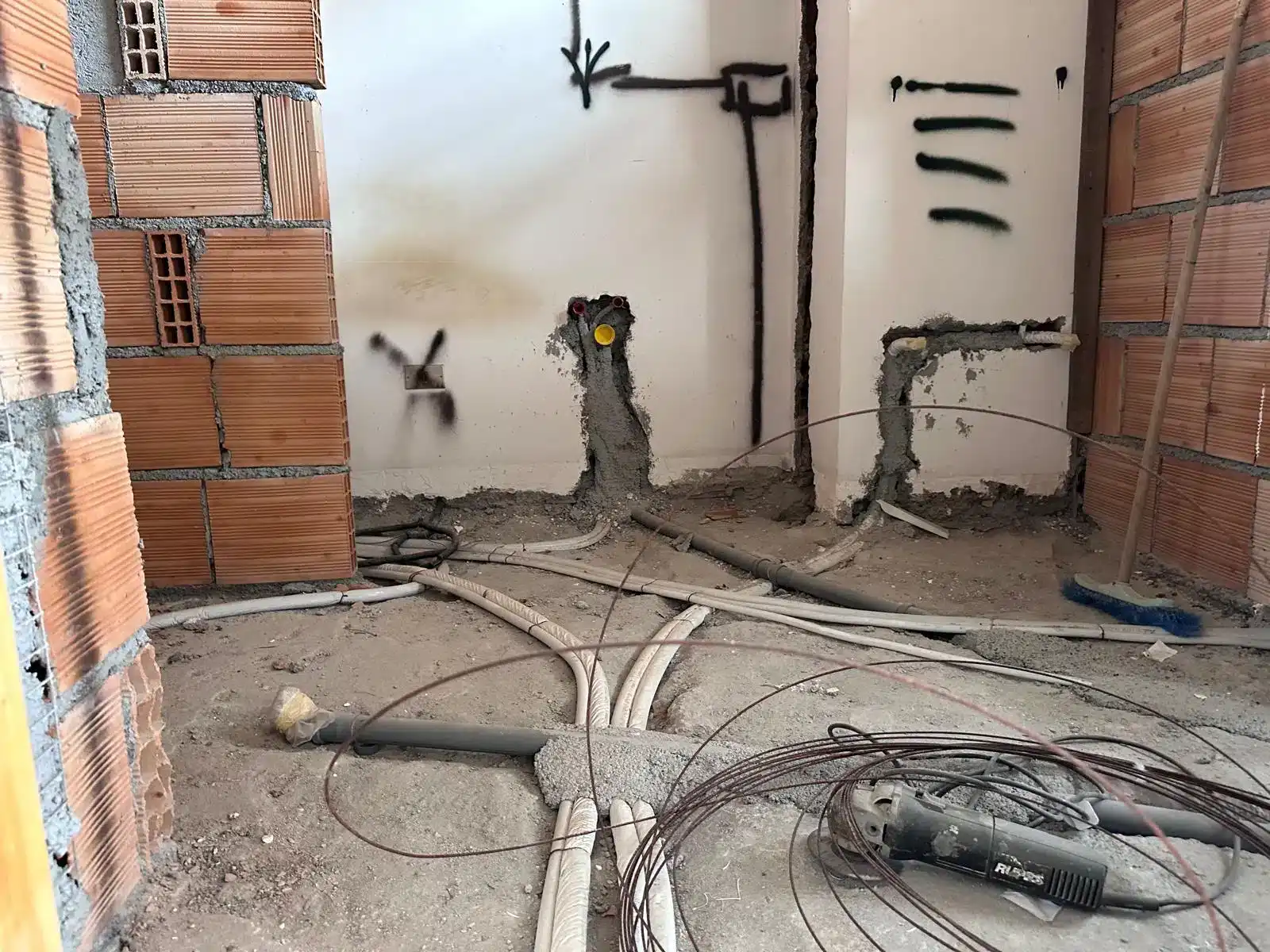 Interno di un appartamento in costruzione con tubature e impianti elettrici visibili.