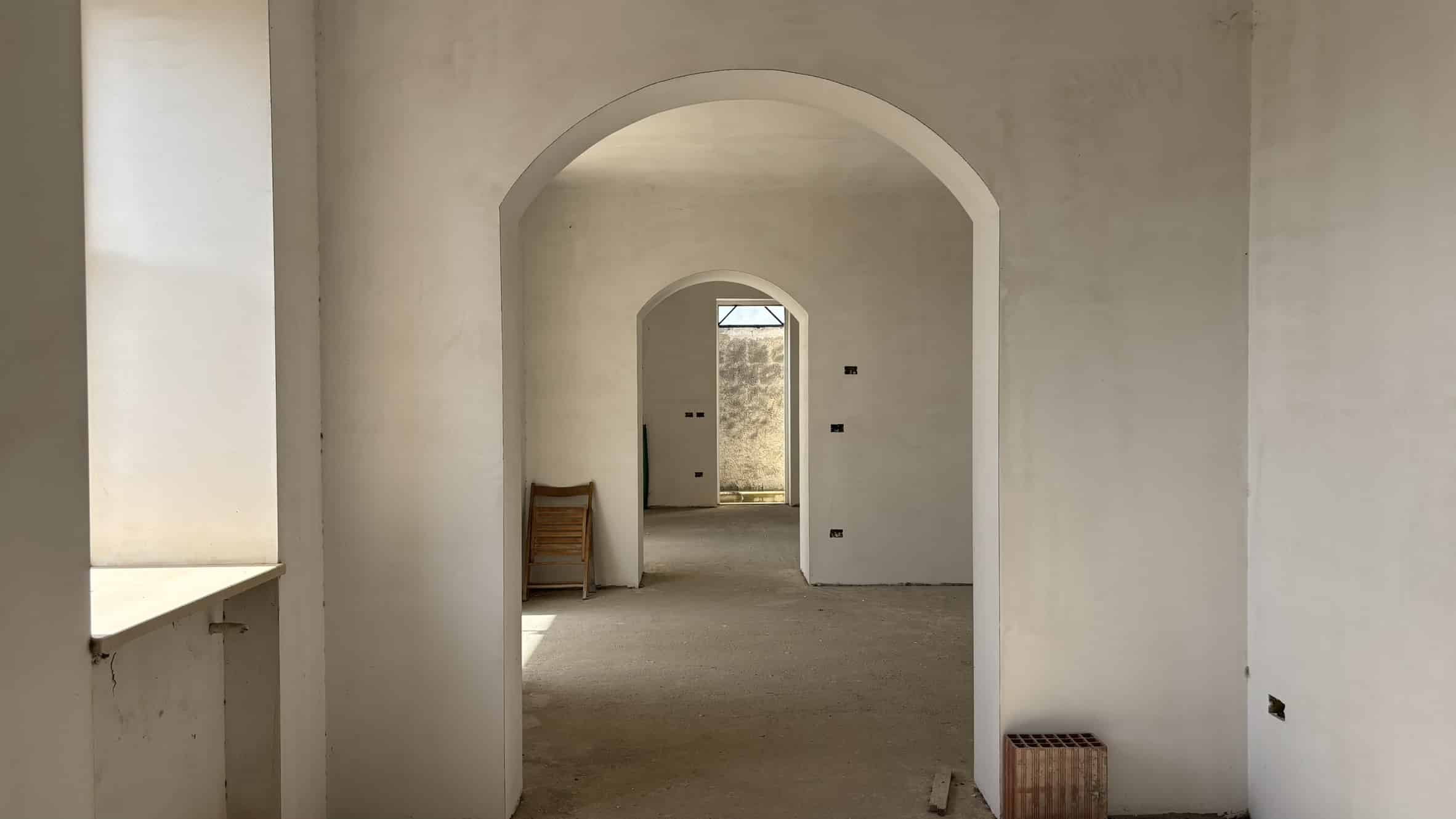 Finestra e pareti interne di una casa in costruzione, ambientazione di un appartamento ancora da completare, con archi e pareti bianche in fase di ristrutturazione, pronti per finiture e arredi.