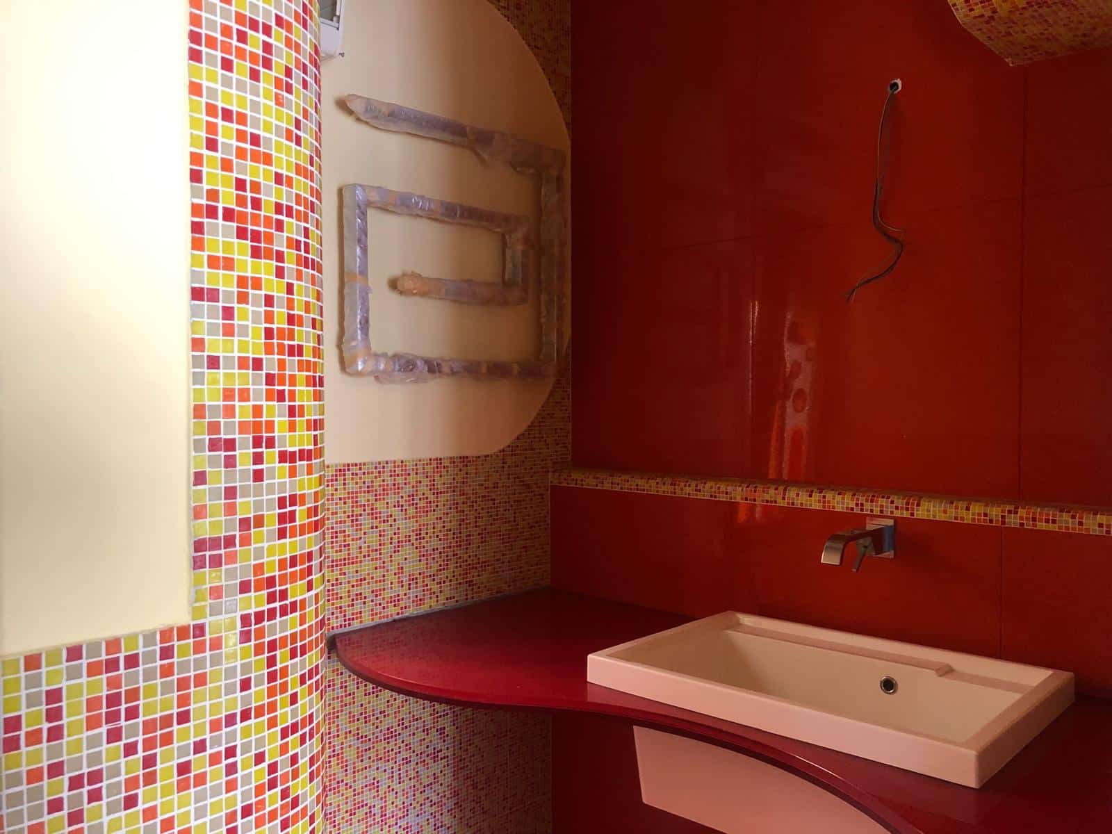 Lavanderia moderna con pareti in mosaico multicolore e finiture eleganti, lavabo bianco e acqua calda, ideale per case di lusso e proprietà di alta qualità.