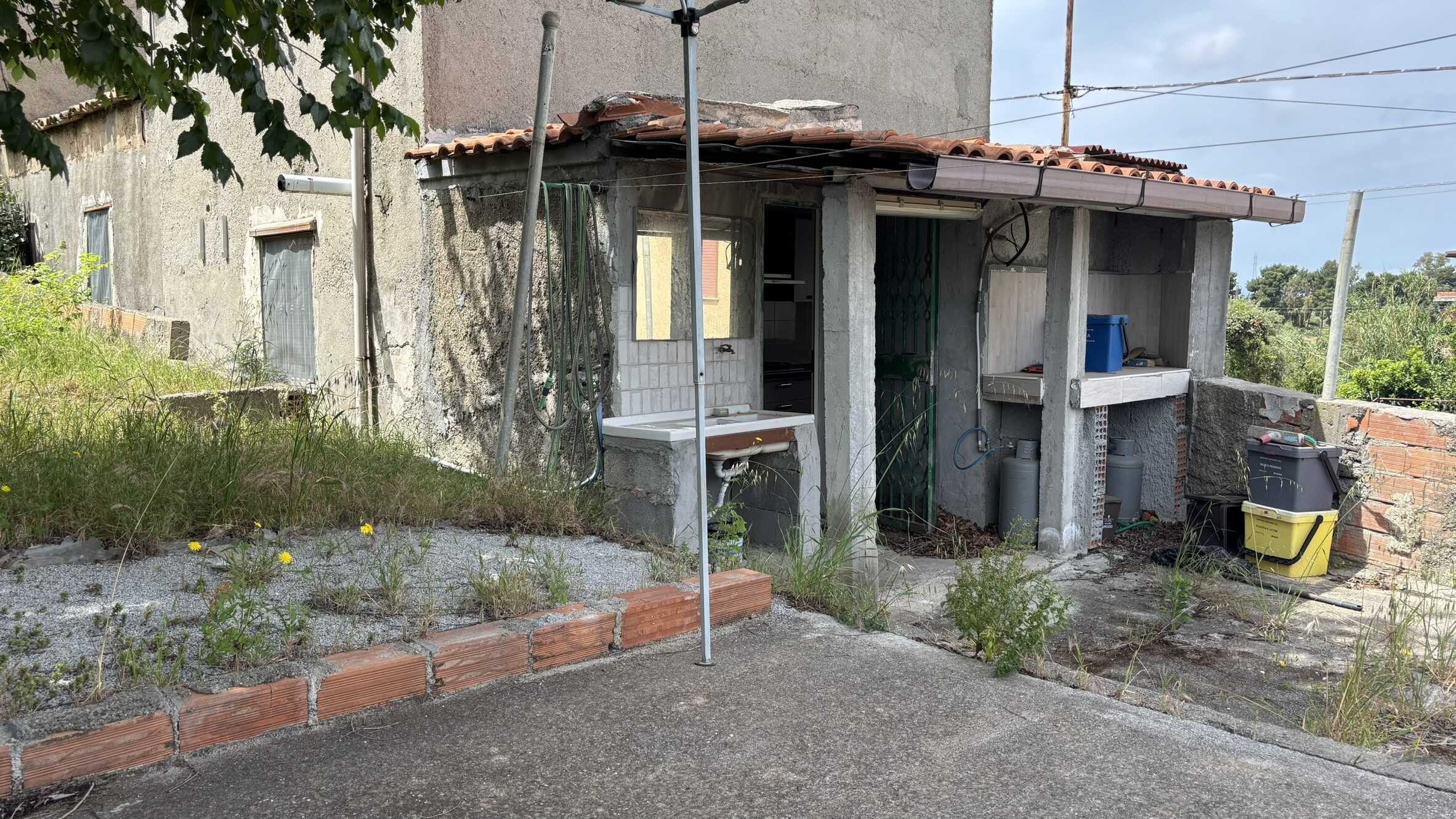 Vecchio spazio esterno di casa in costruzione con lavandino, tubi e attrezzi, ambiente semplice e rustico, perfetto per servizi all'aperto, stile di vita autentico, ristrutturazione possibile.