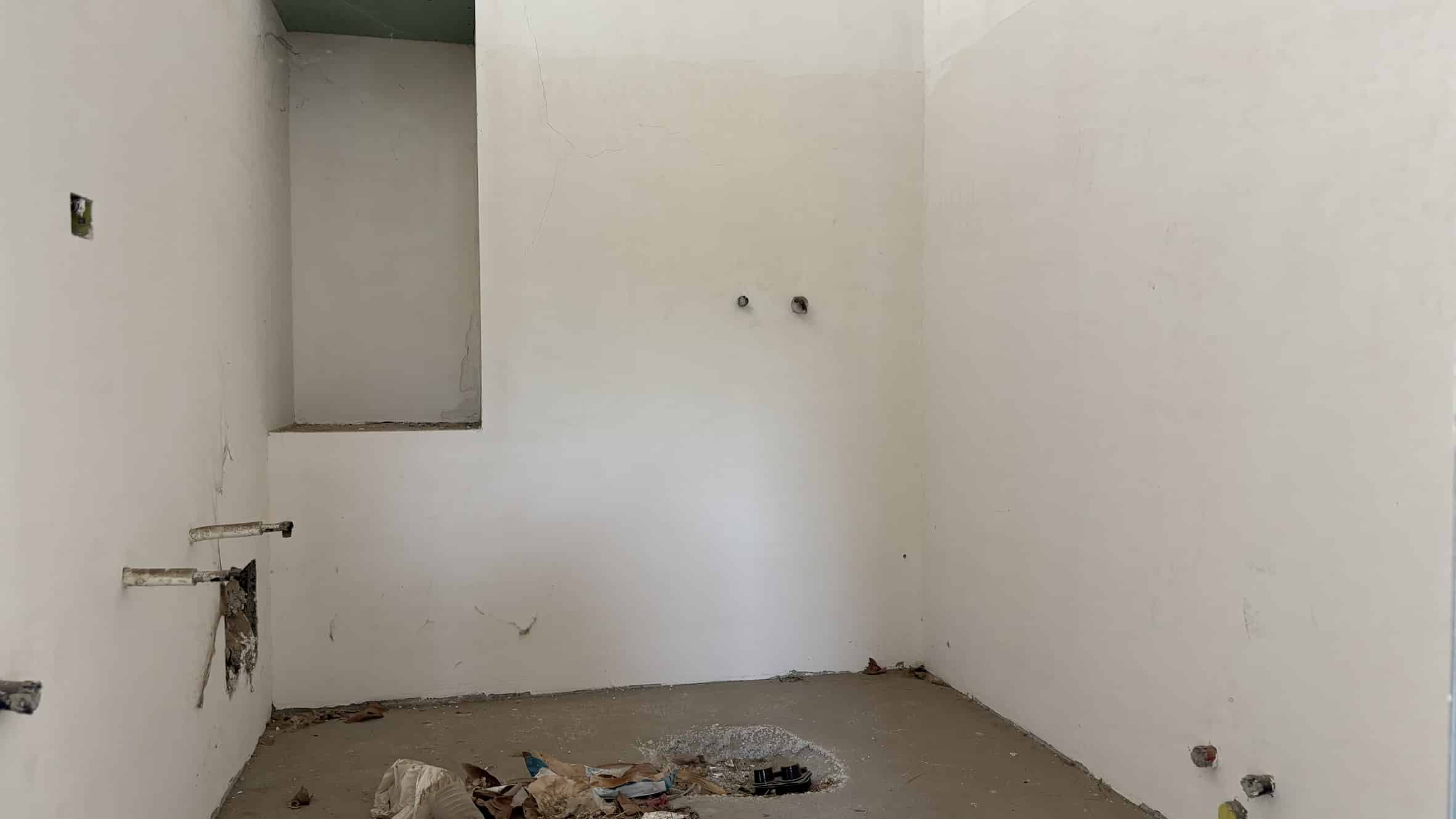 F Nothing in the room has been completed yet, the walls are still unpainted, the pipes are exposed, and there is debris on the floor, indicating ongoing renovation or construction.