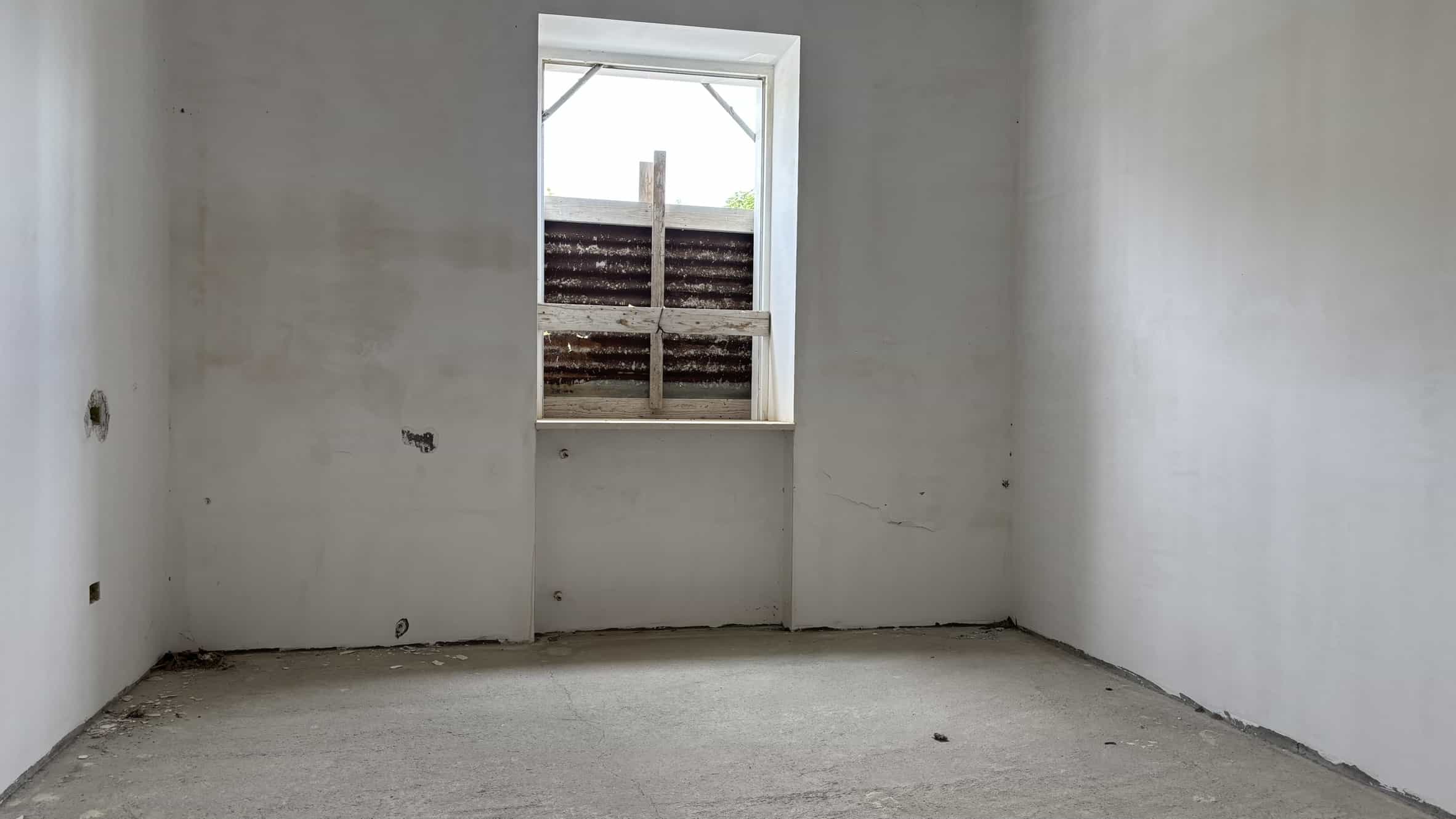 Minimalista stanza in attesa di finiture, con pareti e pavimento ancora da completare, pronta per essere personalizzata, ideale per progetti di costruzione o ristrutturazione casa.