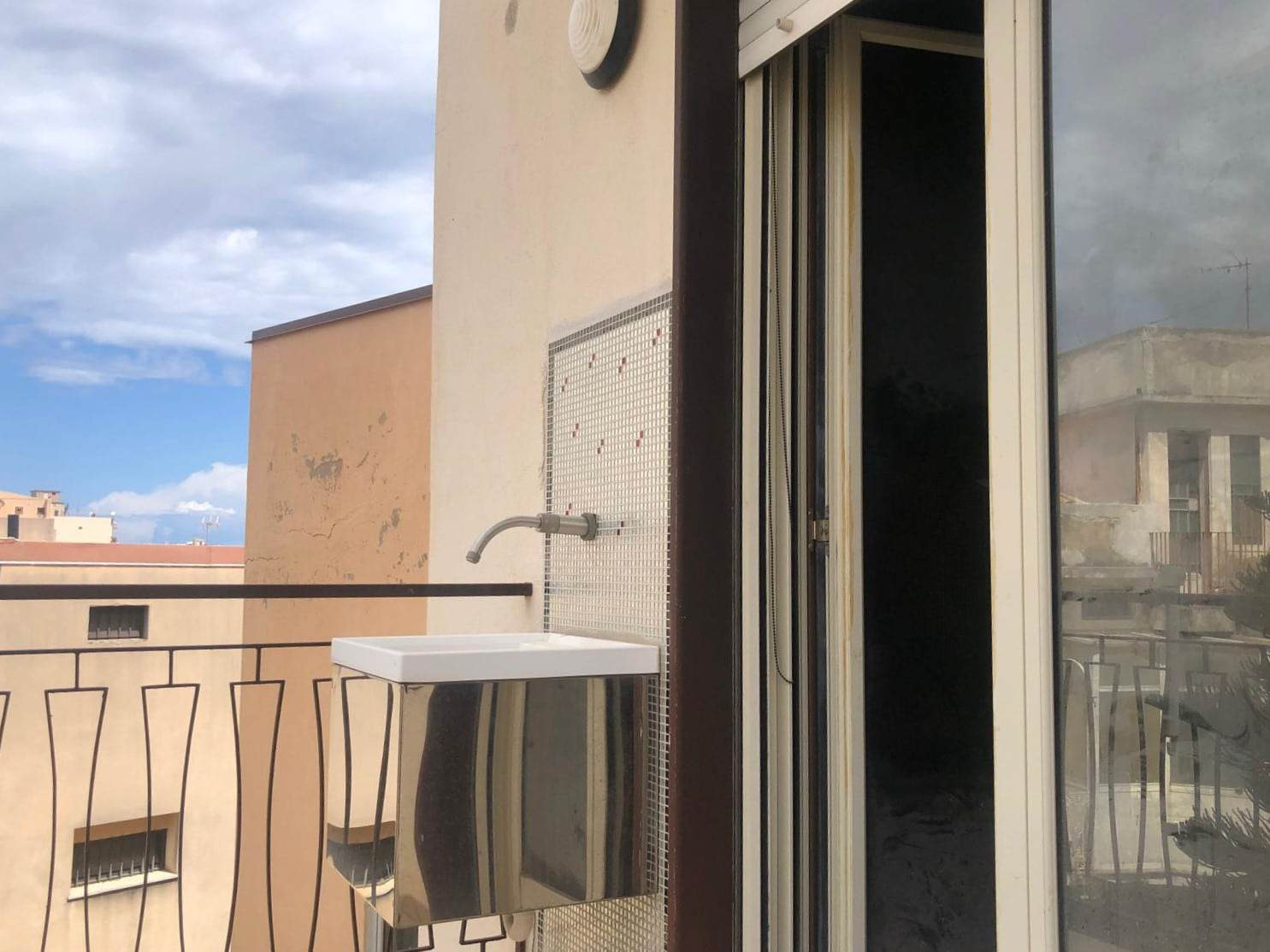 Balcone con lavandino esterno in appartamento, vista su edifici residenziali e cielo nuvoloso, soluzione pratica e funzionale per la gestione dello spazio all'aperto.