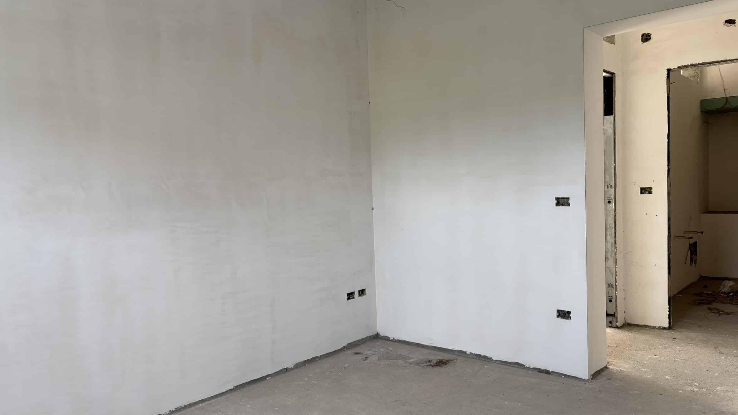 Fondo di una stanza in fase di ristrutturazione con pareti bianche e impianto elettrico in corso, ideale per progetti di edilizia e interior design.