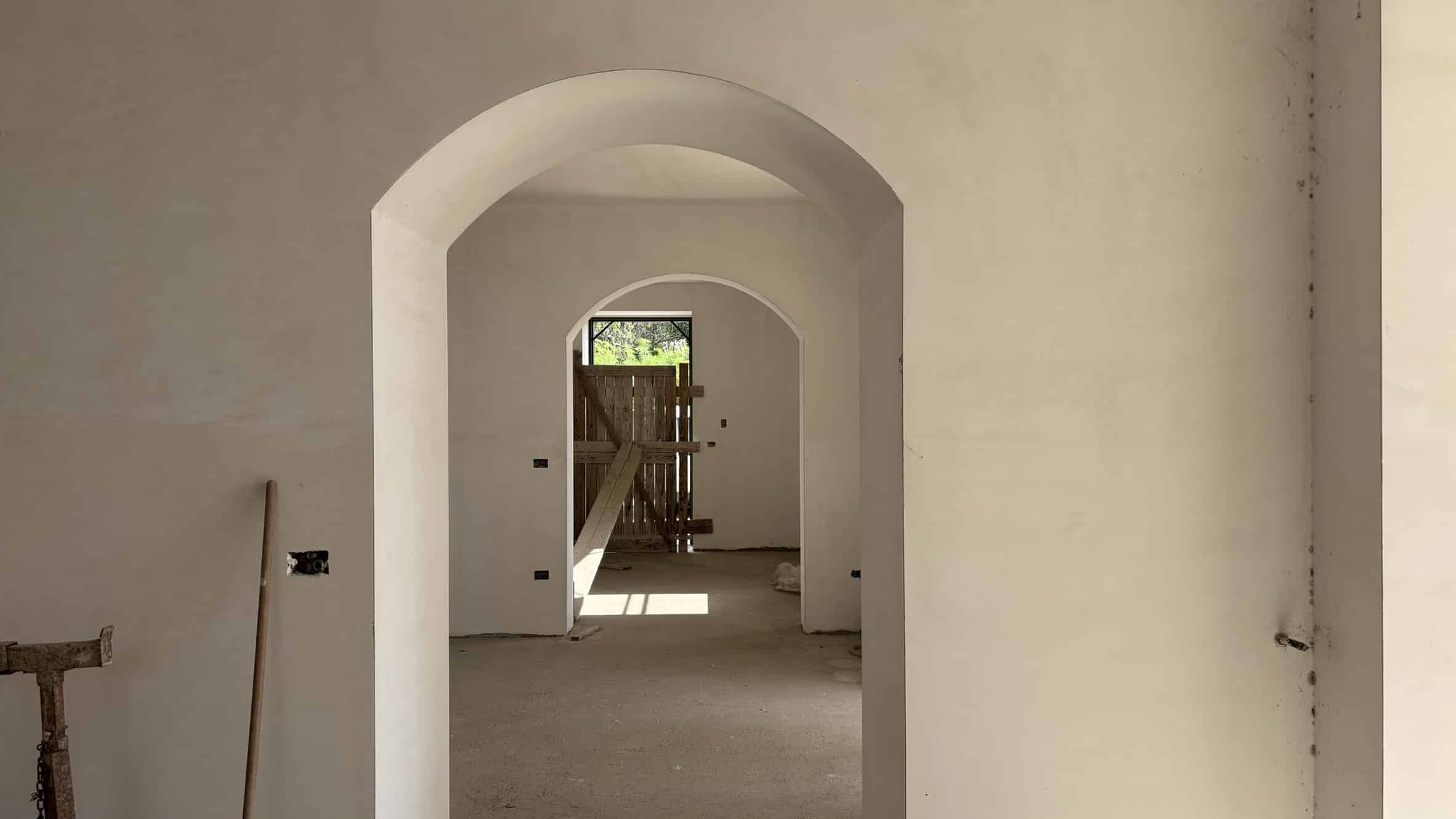 Autore di un immobile in costruzione, pareti interne dipinte di bianco, archi decorativi e apertura verso il giardino con porta in legno. Spazio in fase di ristrutturazione, luminoso e spazioso, ideale per interni moderni e luminosi.