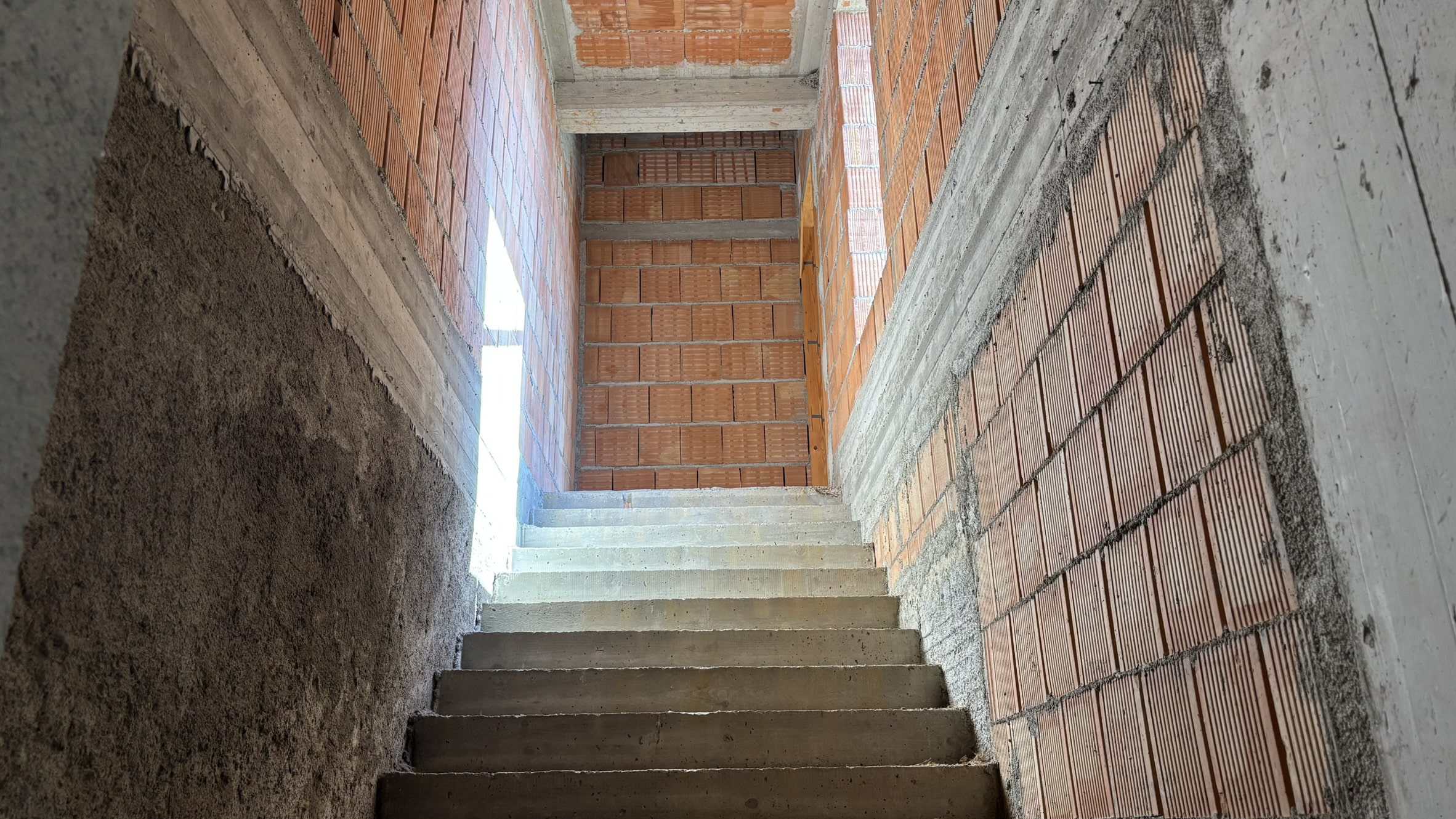 Scala in costruzione con mattoni e cemento, vista dall'alto con finestra per illuminazione naturale.