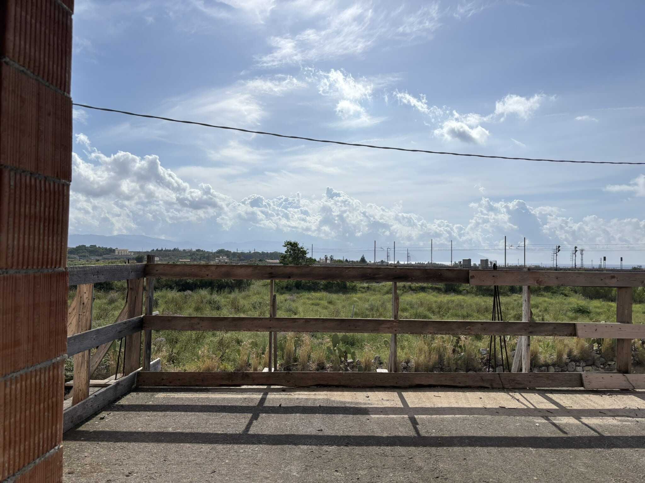 VISTA CAMERA DA BALCONE, TERRAZZA PRIVATA CON BARRIERE IN LEGNO, PAESAGGIO DI CAMPAGNA E CIELO SPIEGATO, COSTRUZIONE IN CEMENTO E MATTONI, TERRA AGRICOLA, AMBIENTE NATURALE, ESPOSIZIONE ALL'ARIA APERTA.