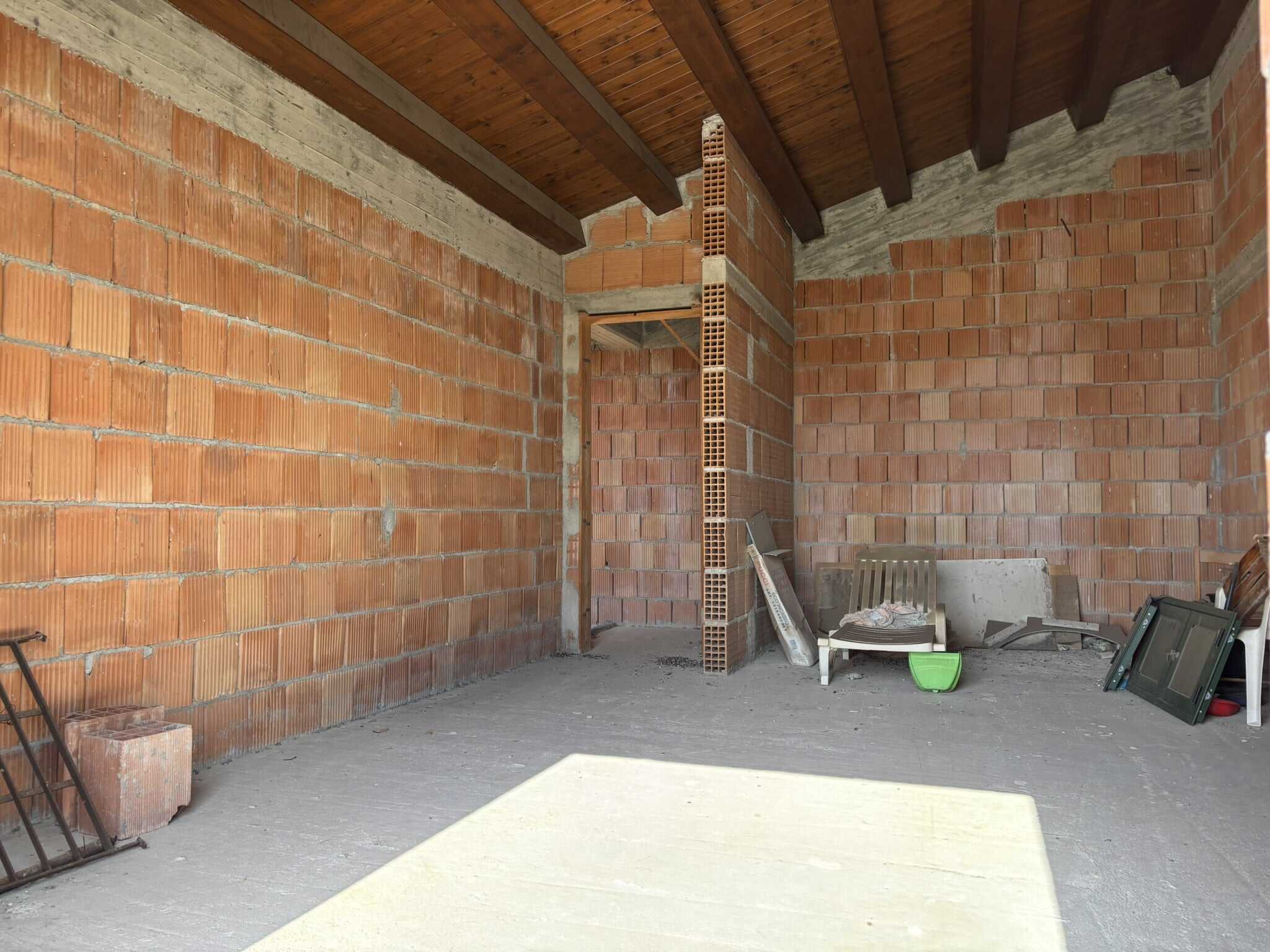 Finestra di un edificio in fase di costruzione con pareti in mattoni e soffitto in legno, materiali edili e attrezzi da lavoro visibili, immagine di una casa in costruzione NextCasa.