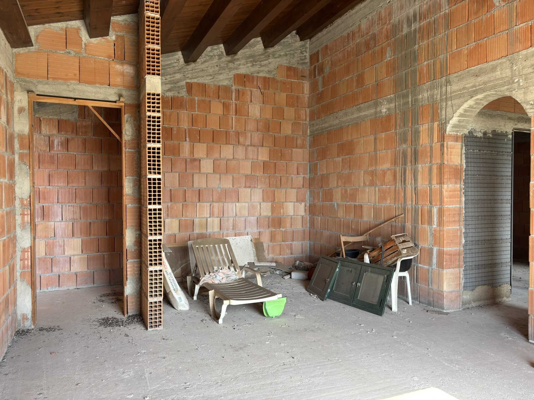 Blocchi di mattoni rossi e pareti in costruzione, elementi di arredo da esterno tra cui sedie di plastica e piccoli materiali da cantiere, ambientazione di un edificio in fase di realizzazione, immagini di costruzione residenziale.