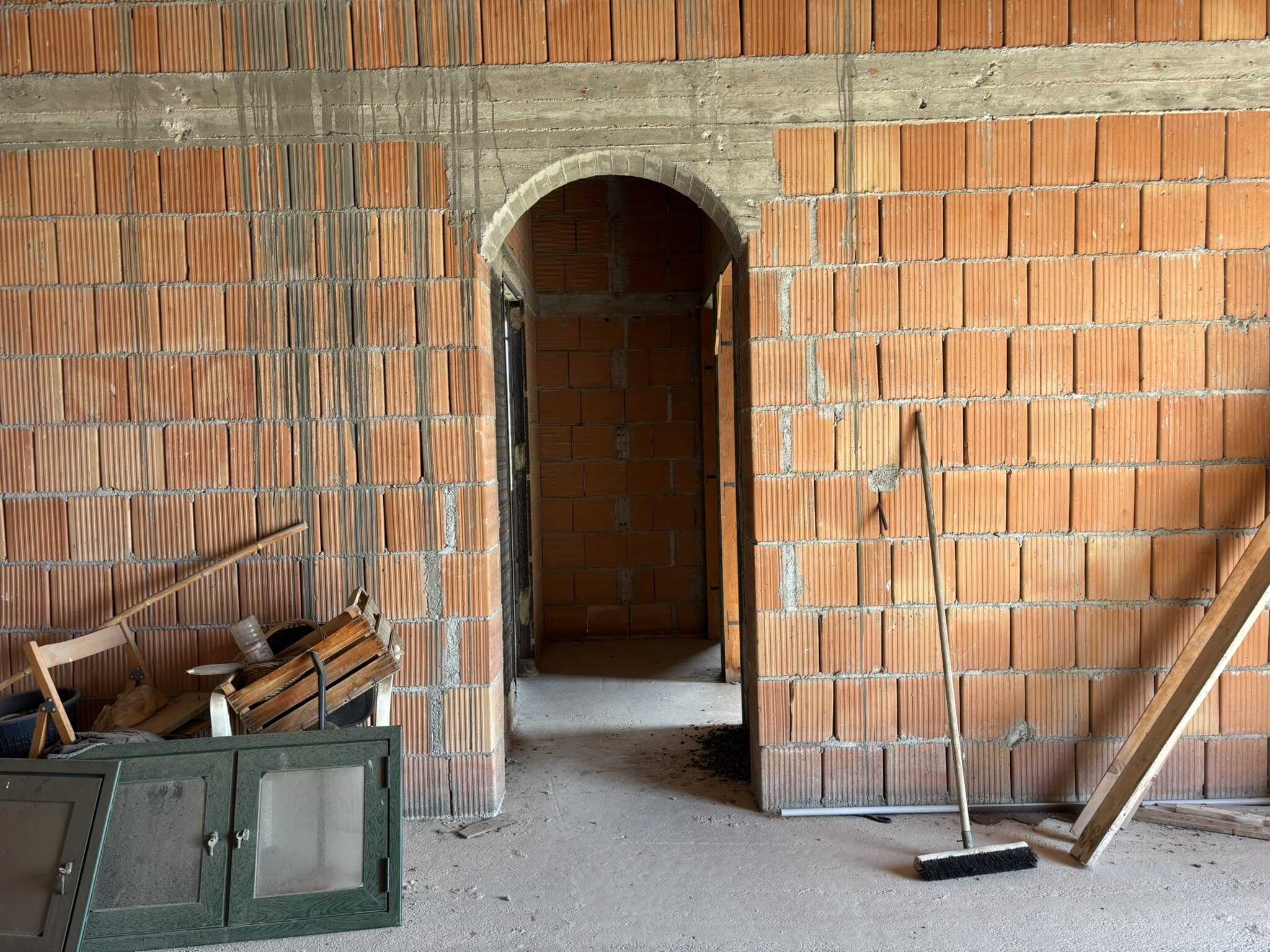 Parete in mattoni rossi con arco in muratura, ambienti in costruzione, strumenti da lavoro e materiali edilizi.