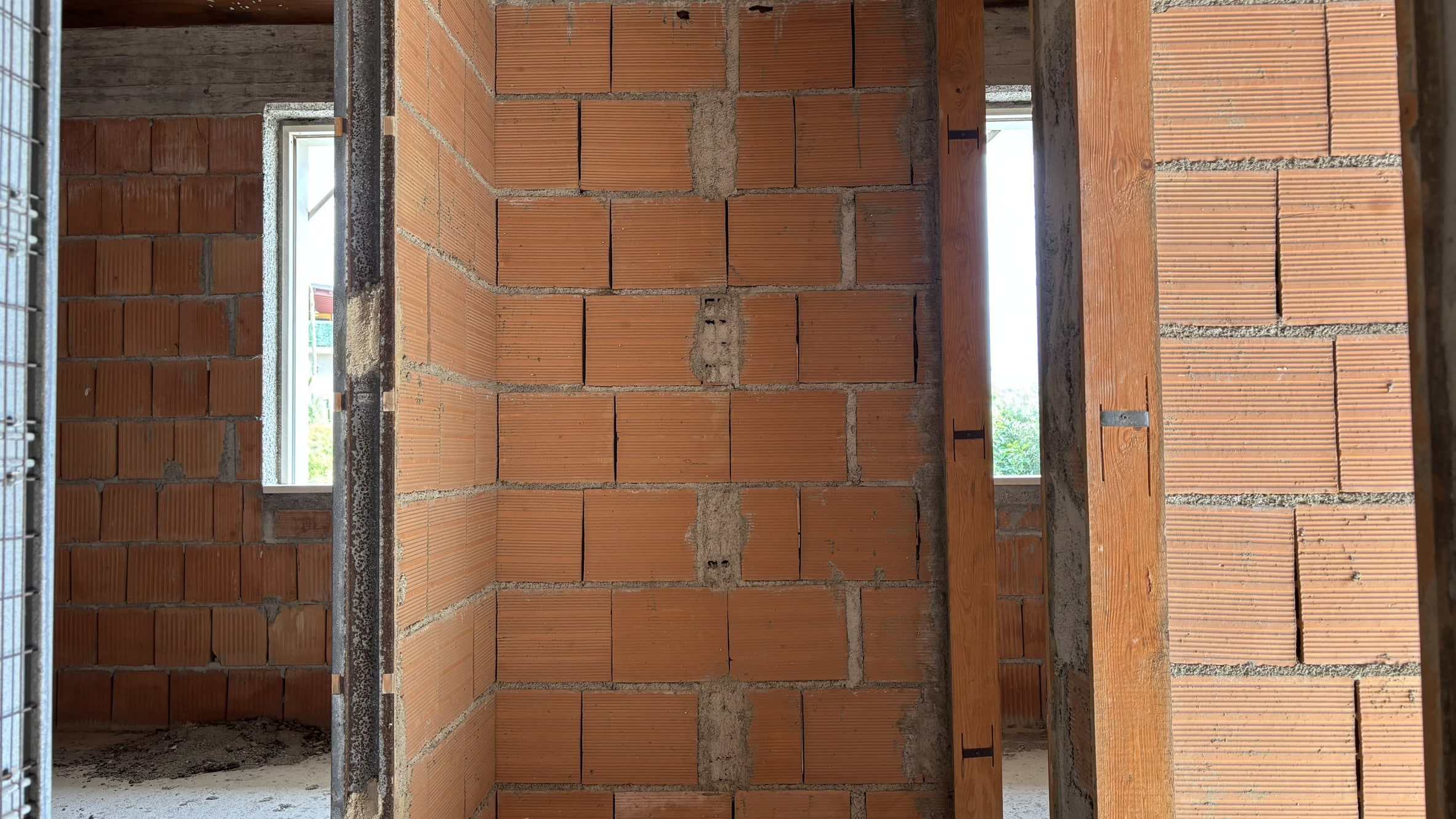 Parete in mattoni a vista in fase di costruzione, vista interna di un edificio in costruzione con finestre e strutture in legno.