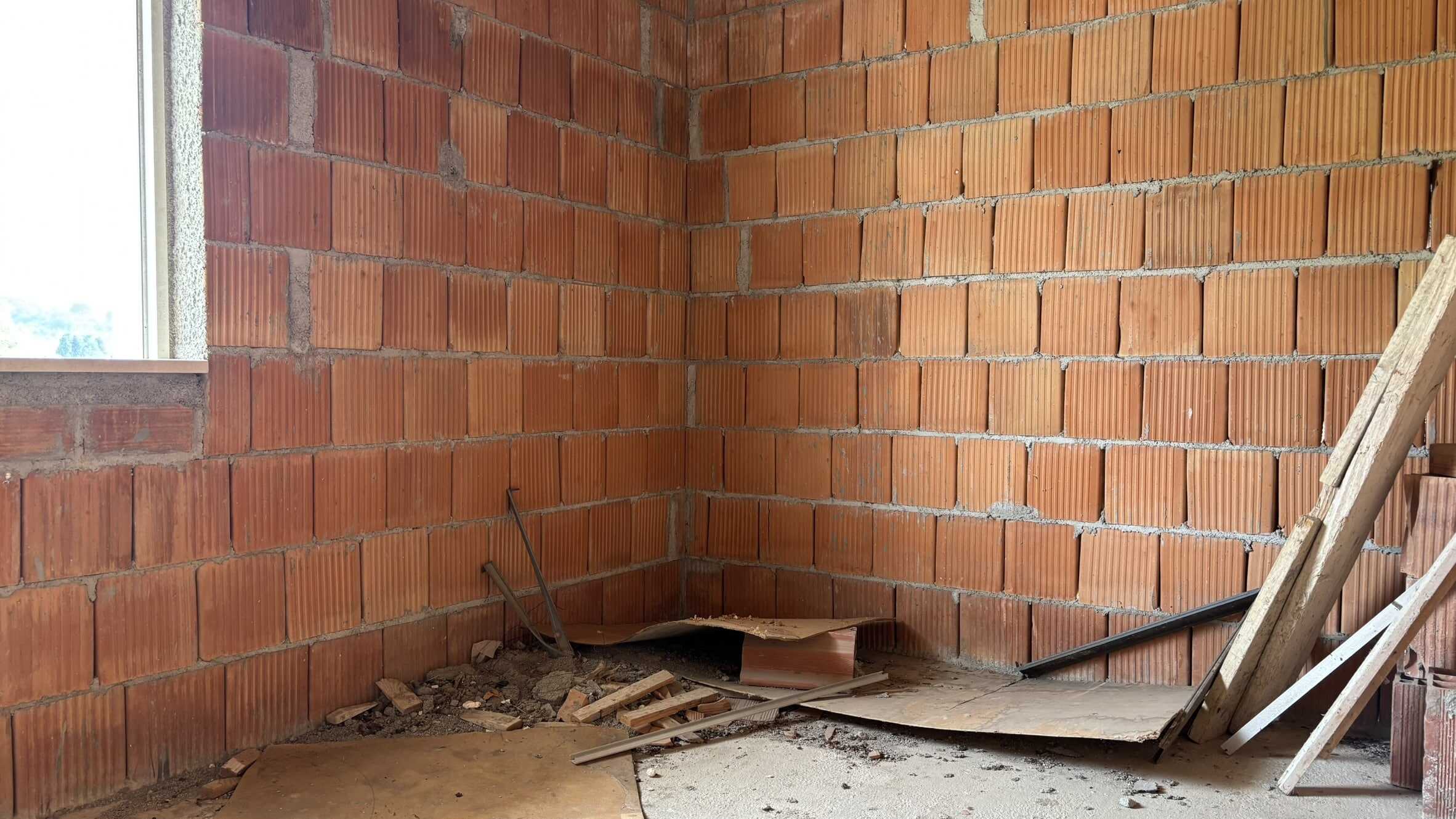 Parete interna in mattoni rossi in costruzione, finestra con luce naturale, cantiere edile con attrezzi e materiali, ideale per foto di ristrutturazione e costruzione edilizia.