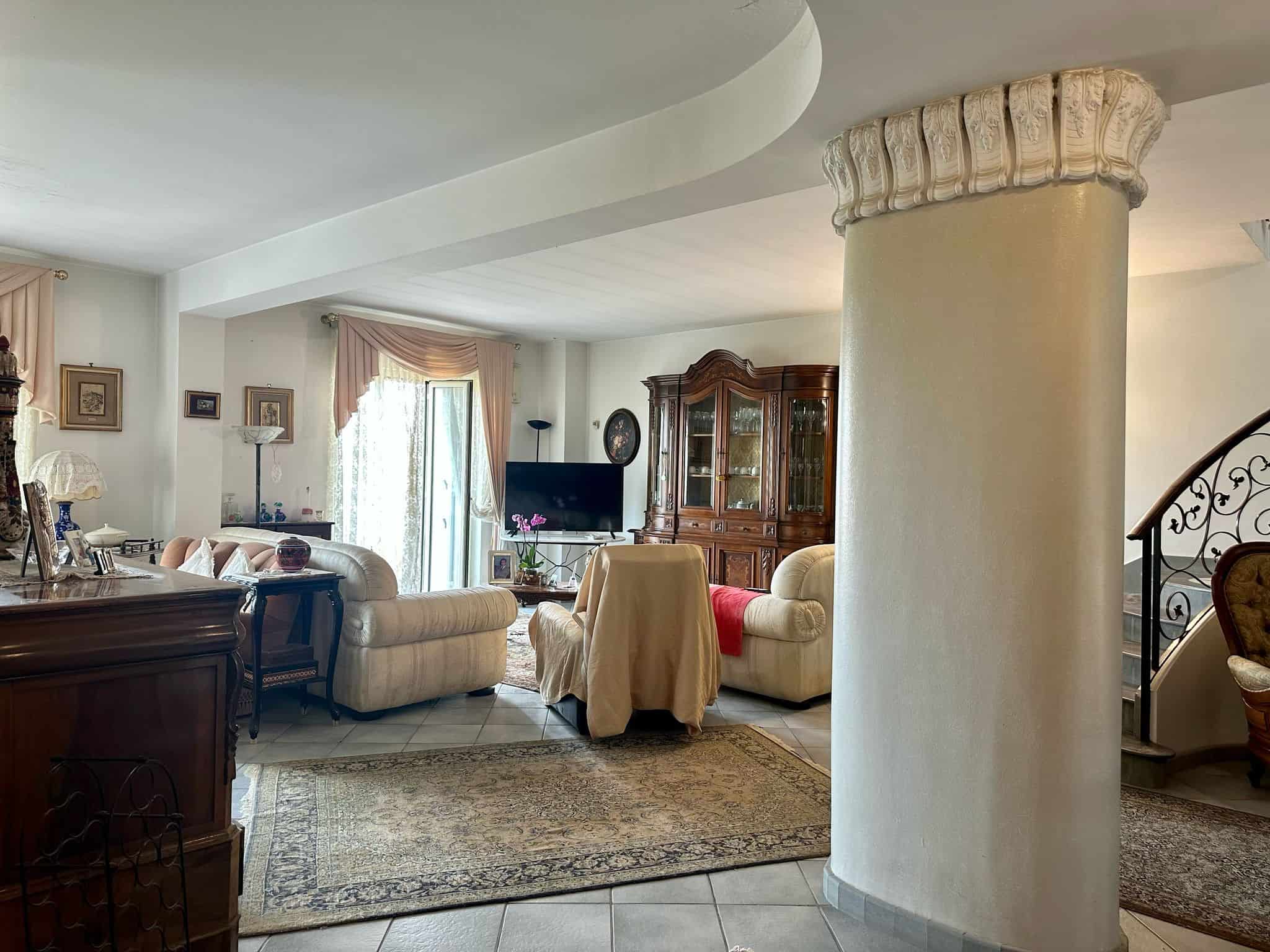Accogliente zona giorno arredata con divani in tessuto beige, mobili classici, e dettagli eleganti, ideale per il relax e l'intrattenimento in un ambiente luminoso e spazioso.