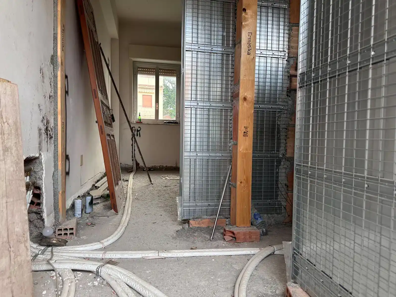 Interno di una casa in fase di ristrutturazione con strutture in metallo e tubature visibili, pronto per lavori di finitura.