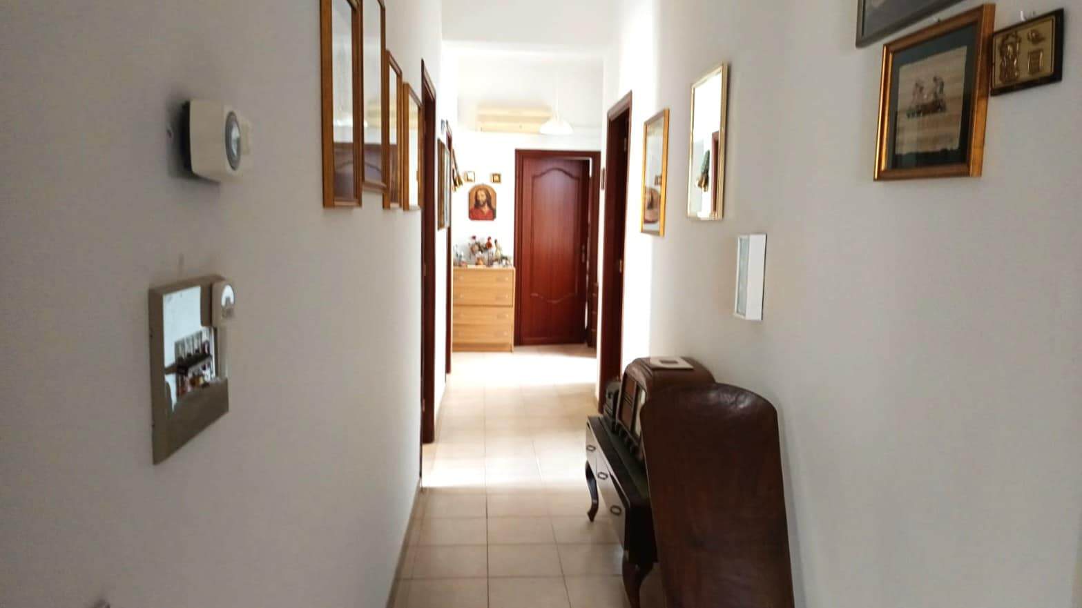 Elegante corridoio di casa con parete decorata con quadri e immagini sacre, pavimento in ceramica e porta d'ingresso in legno, ambiente luminoso e accogliente perfetto per interni di proprietà residenziali.