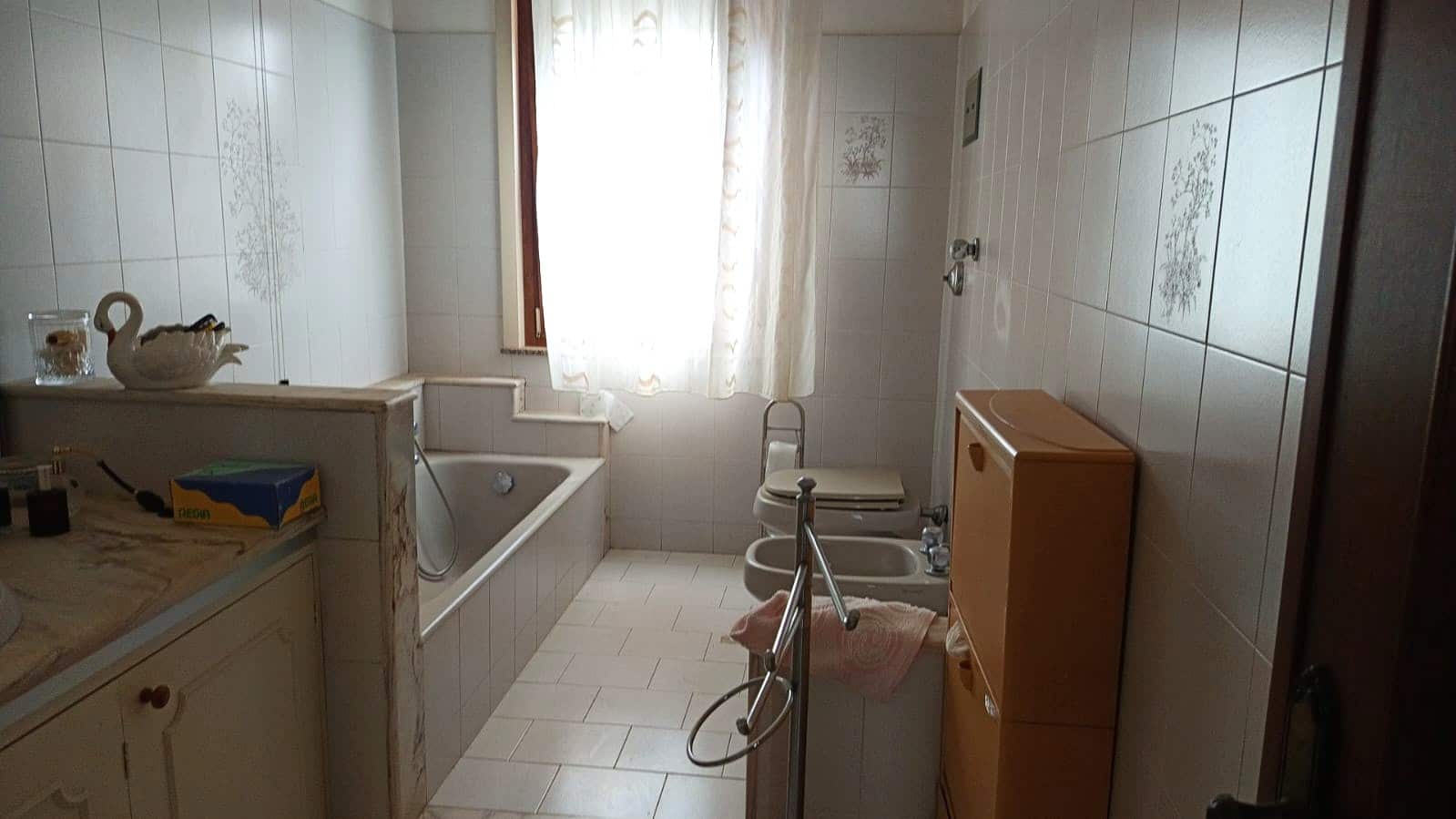Lavanderia con vasca da bagno, bidet e finestra con tende a raso, arredi in legno. Spazio funzionale e luminoso, ideale per le esigenze di casa. Perfetta per servizi di lavanderia e relax domestico.