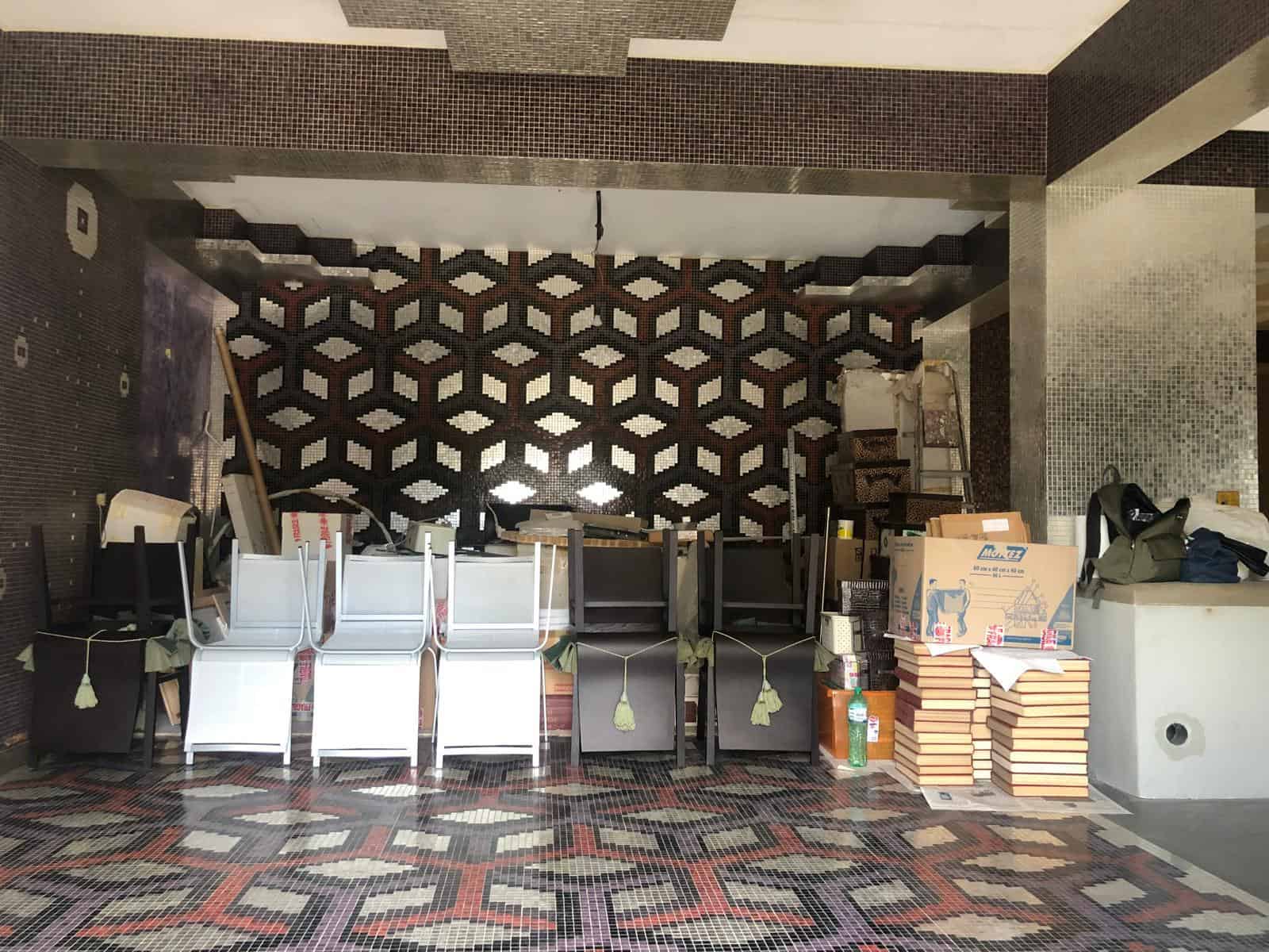 Spazio di lavoro o area commerciale in fase di allestimento con sedie, scatole e materiali, pavimentazione e pareti con dettagli di mosaico.