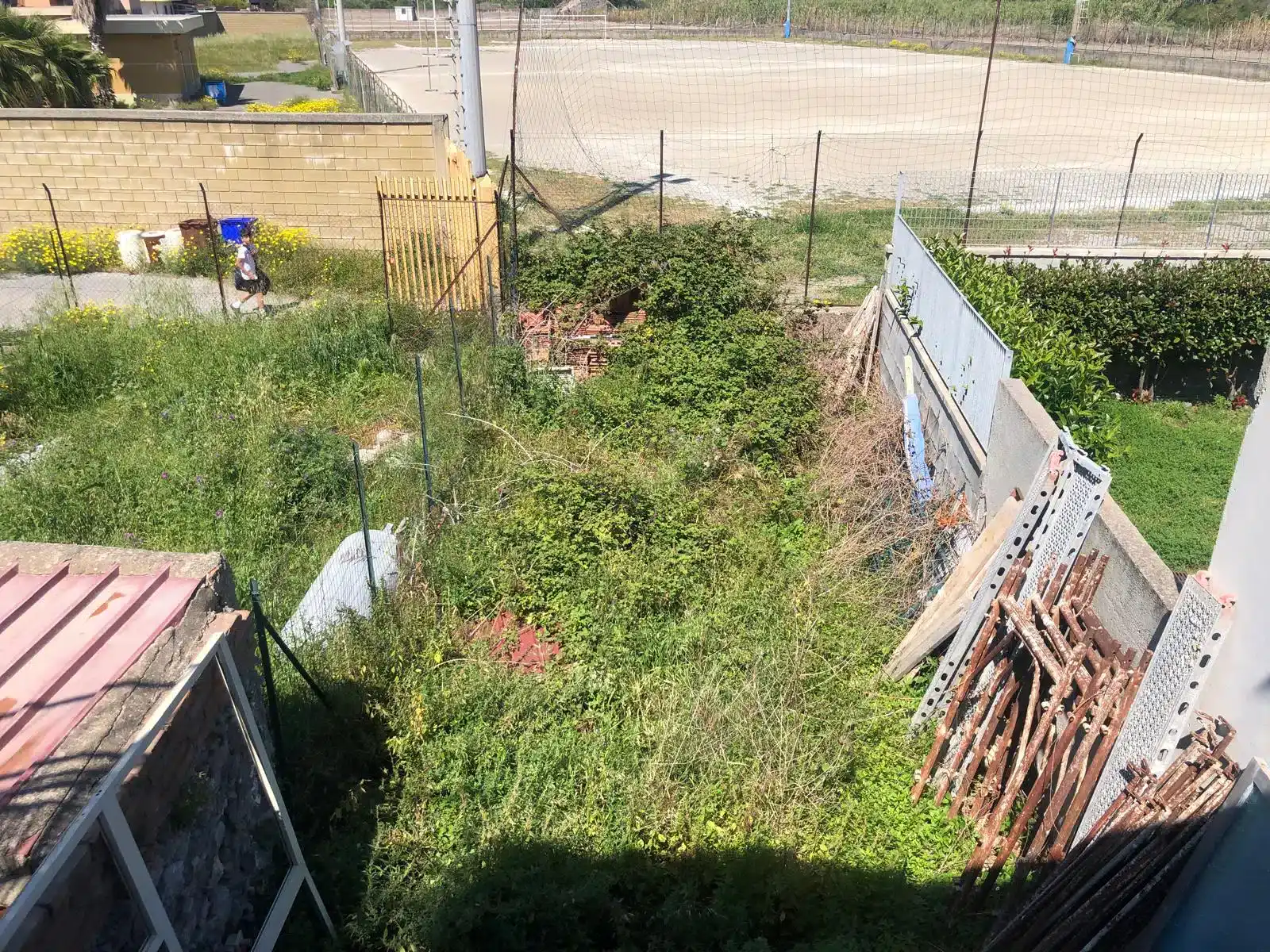 Spazio esterno di una casa indipendente in vendita a Milazzo, con prato verde, recinzione e alcuni materiali da costruzione.