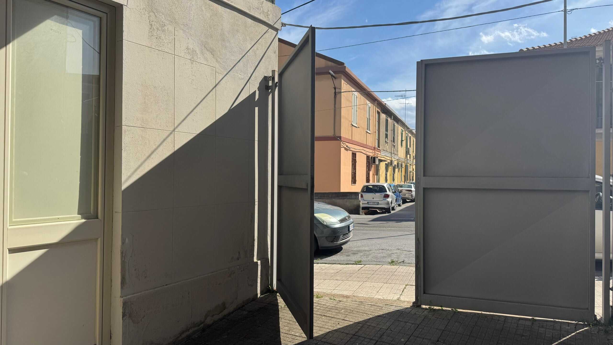 Porta di ingresso bifold all'aperto in zona urbana, prospettiva dalla strada con edifici e auto, stile moderno e funzionale, ambiente residenziale e commerciale, sicurezza e praticità per accesso all'abitazione, fotografia di alta qualità, luce naturale.