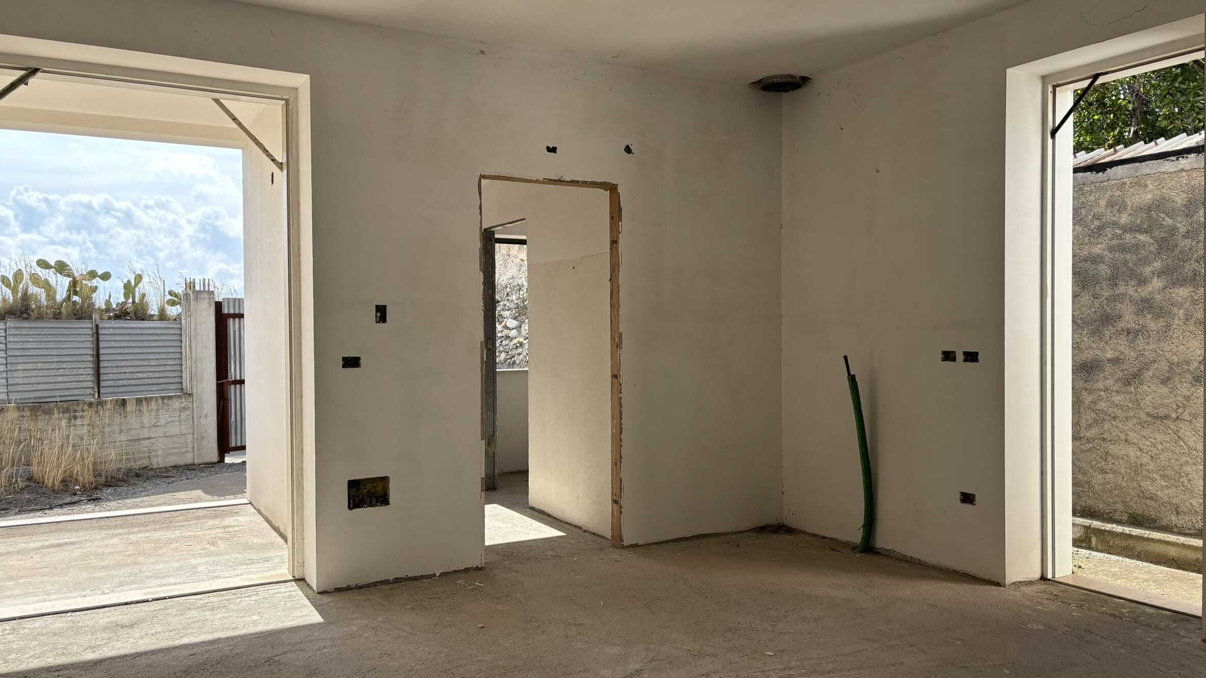 Progetto di ristrutturazione di interni di una casa moderna in fase di costruzione, con pareti a cemento grezzo e grandi aperture per porte e finestre, pronto per personalizzazione e arredamento.