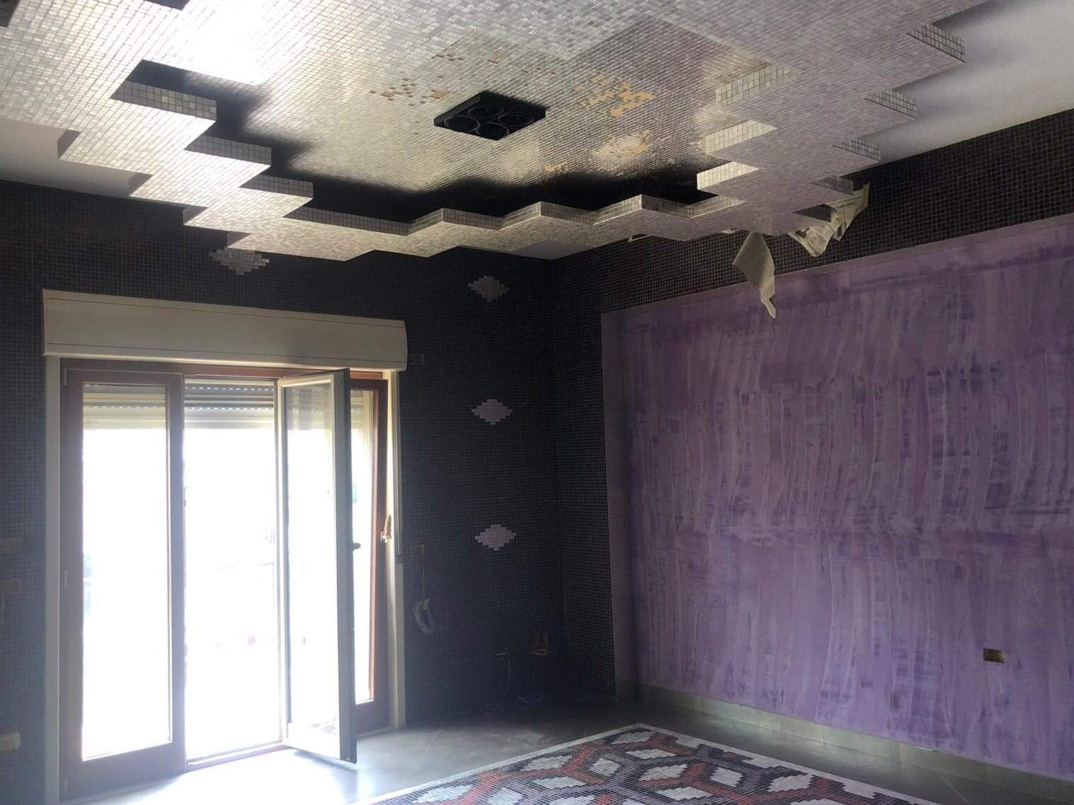 Interruttore della luce in un appartamento in fase di ristrutturazione con pareti viola e soffitto decorato in mosaico, con accesso a balcone o terrazza.