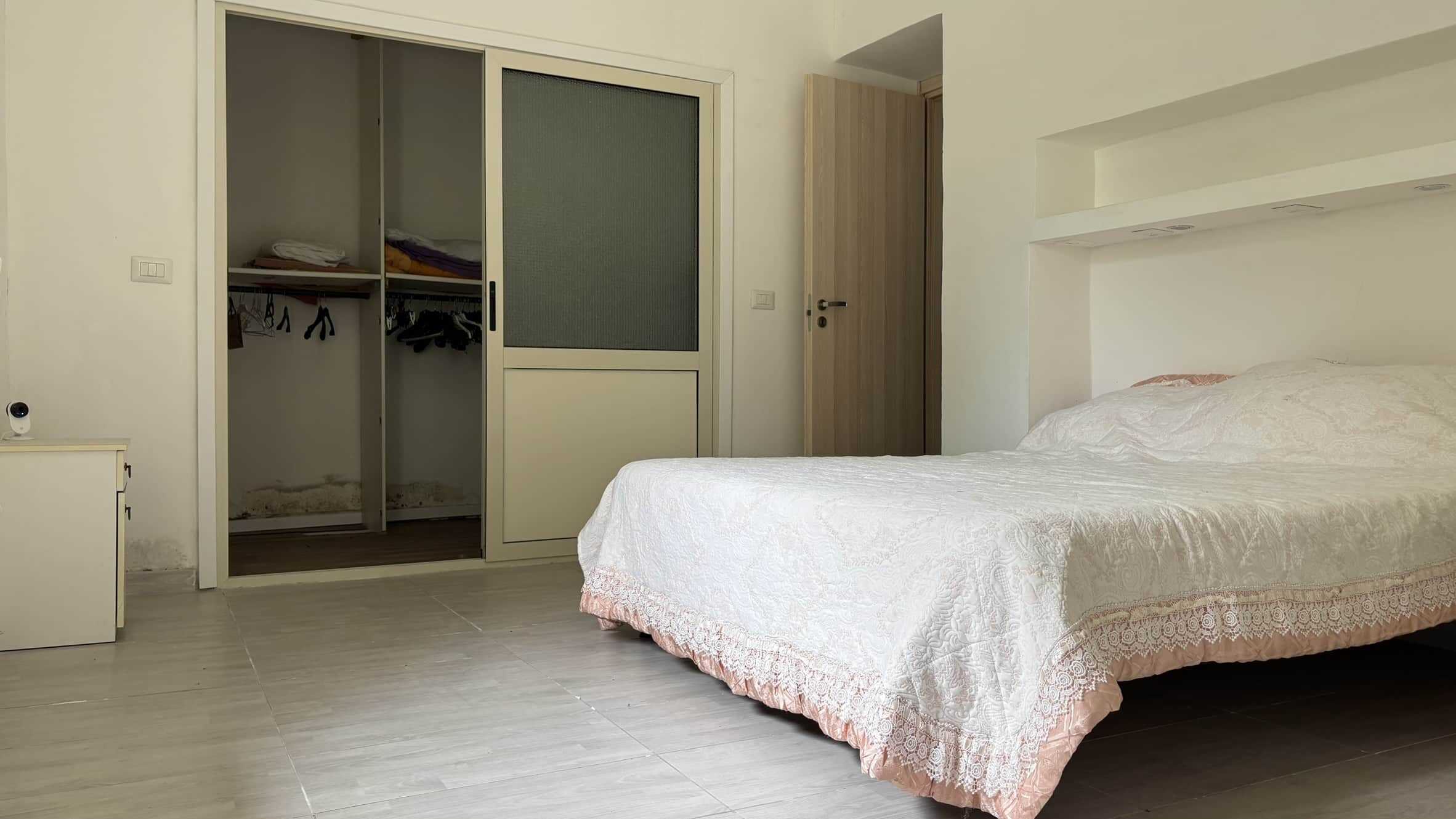 Armadio a due ante scorrevoli con spazio per vestiti e scarpe, letto matrimoniale con copriletto bianco e decorativo rosa, ambiente luminoso e ben organizzato casa in affitto o vendita NextCasa.