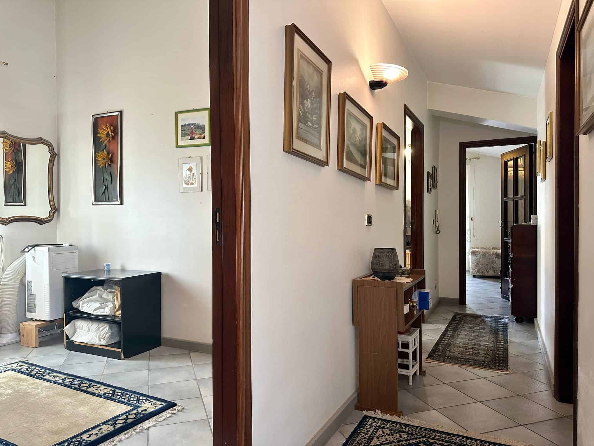 Doppio scatto di un corridoio e ingresso di una casa con pareti attrezzate e decori vintage, arredamento funzionale e tappeti eleganti, ambiente accogliente e ben illuminato.