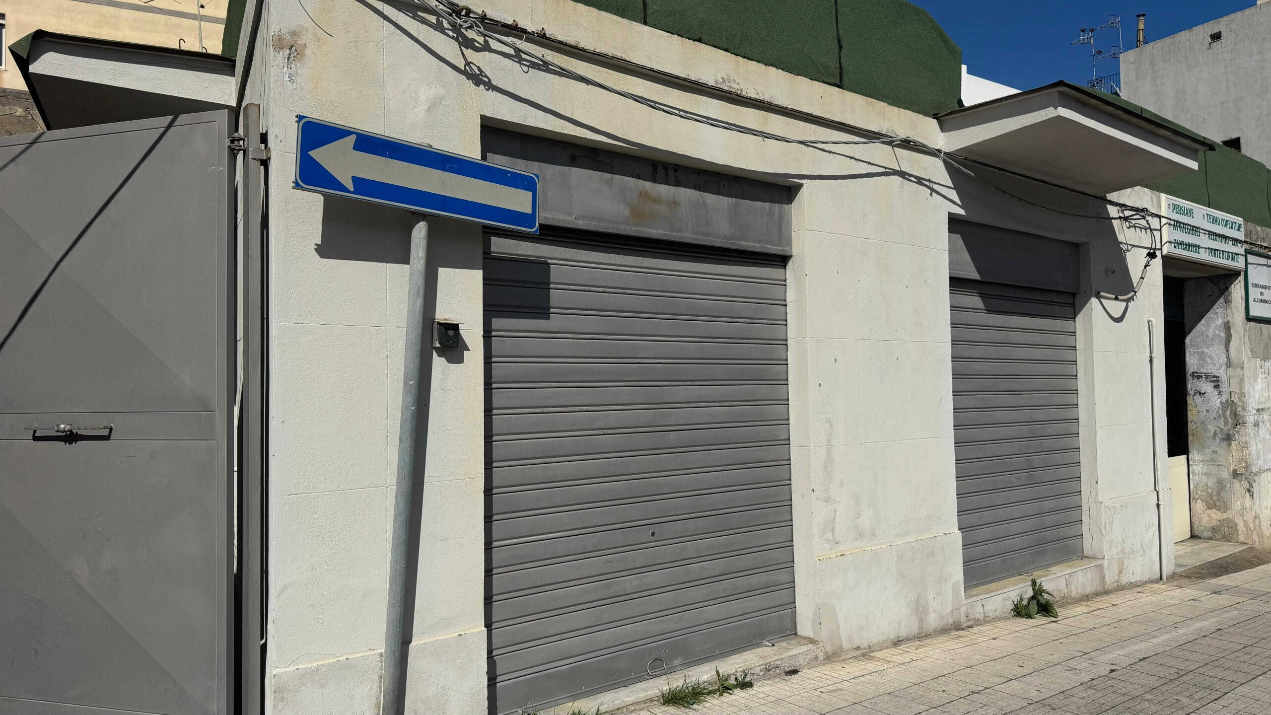 Cancelletto di sicurezza esterno con serranda automatica in alluminio, fronte strada in zona urbana, dettagli di sicurezza e persiane blindate.