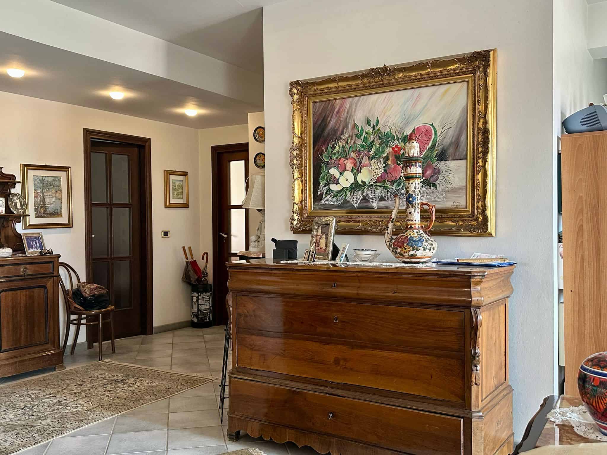 Elegante ingresso con arredi in legno, dipinti alle pareti e dettagli decorativi di stile classico. Atmosfera accogliente e raffinata in un ambiente domestico ben arredato.
