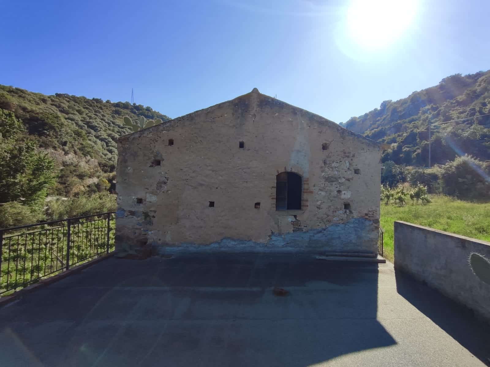 Vecchio edificio in pietra in stile rustico circondato da montagne verdi e cielo sereno, ideale per proposte di ristrutturazione e investimento immobiliare, immerso in un suggestivo paesaggio naturale.