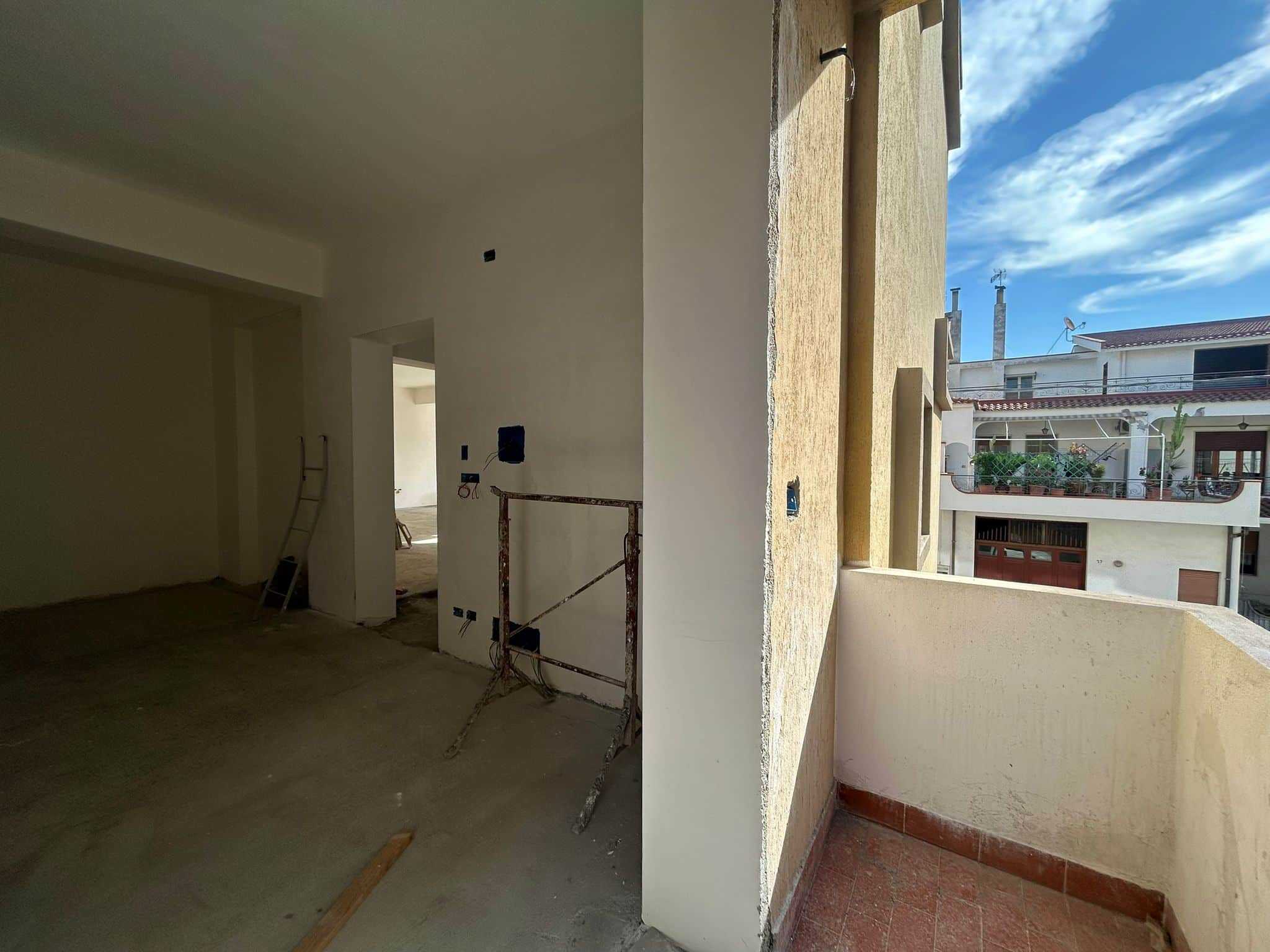 Camera in costruzione con balcone, ambienti di nuova ristrutturazione, vista sull'edificio circostante, luce naturale, progetto di casa moderna NextCasa.