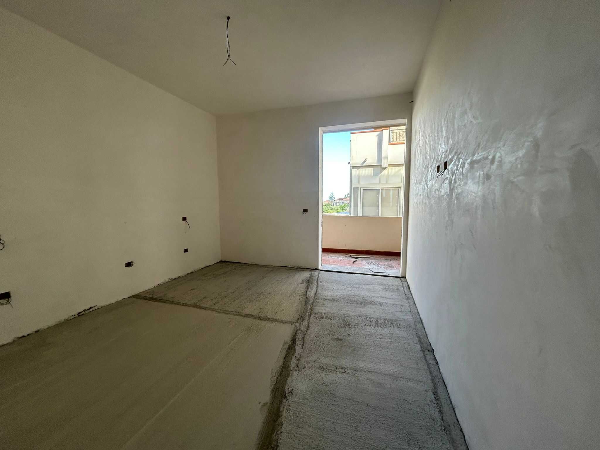 Interni di un appartamento in fase di ristrutturazione, con pareti bianche, pavimenti in fase di finitura e balcone con vista sulla città.