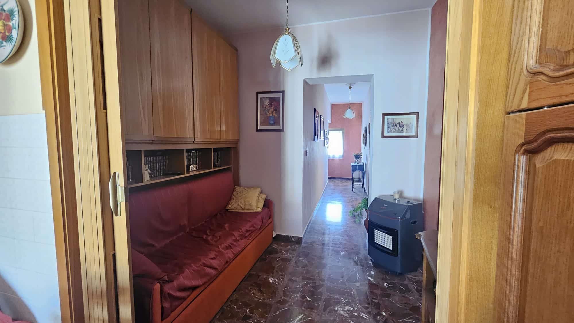 Divano letto rosso in soggiorno con libreria in legno e pareti decorate con quadri, ingresso spazioso con pavimento in marmo e calorifero, stile classico, illuminazione da plafoniera.