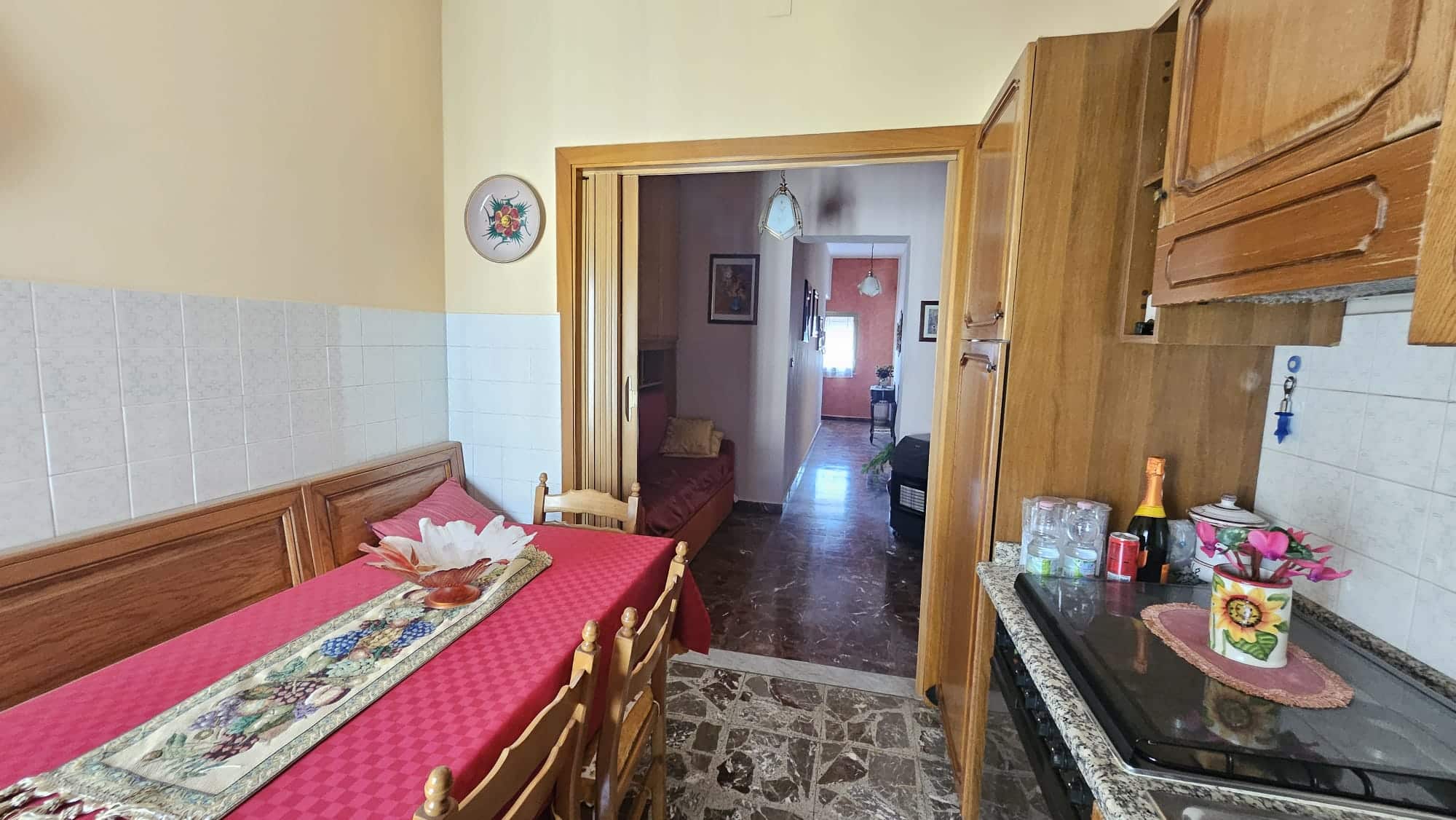 Accesso alla zona pranzo e cucina di una casa tradizionale con mobili in legno e dettagli decorativi floreali. Ambienti accoglienti ideali per la vita quotidiana e momenti conviviali.