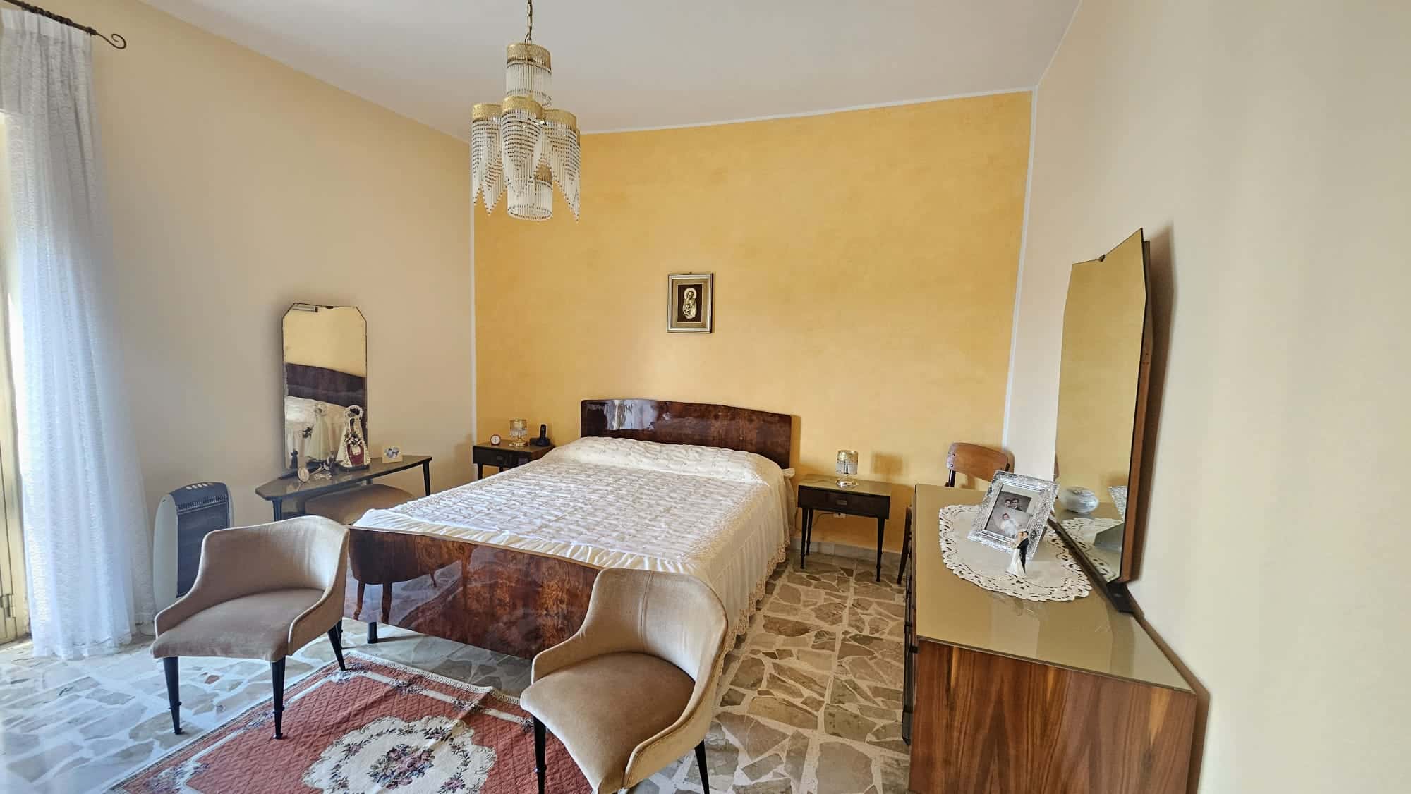 Letto matrimoniale con testiera in legno, arredamento classico, camera da letto luminosa con mobili in stile vintage, dettagli eleganti e decorazioni vintage.