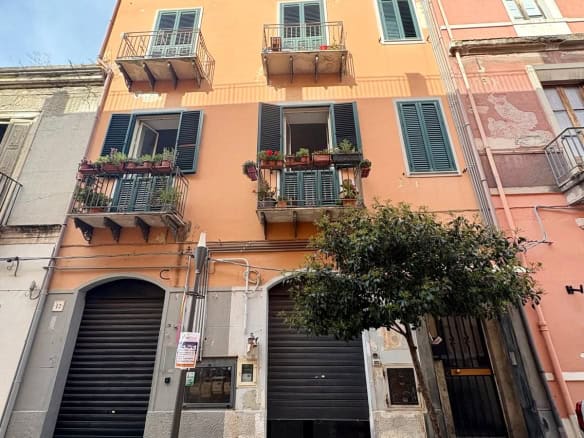 Vicolo con edificio residenziale di charme, caratteristiche balconate con piante, finestre con persiane verdi, atmosfera autentica e accogliente.