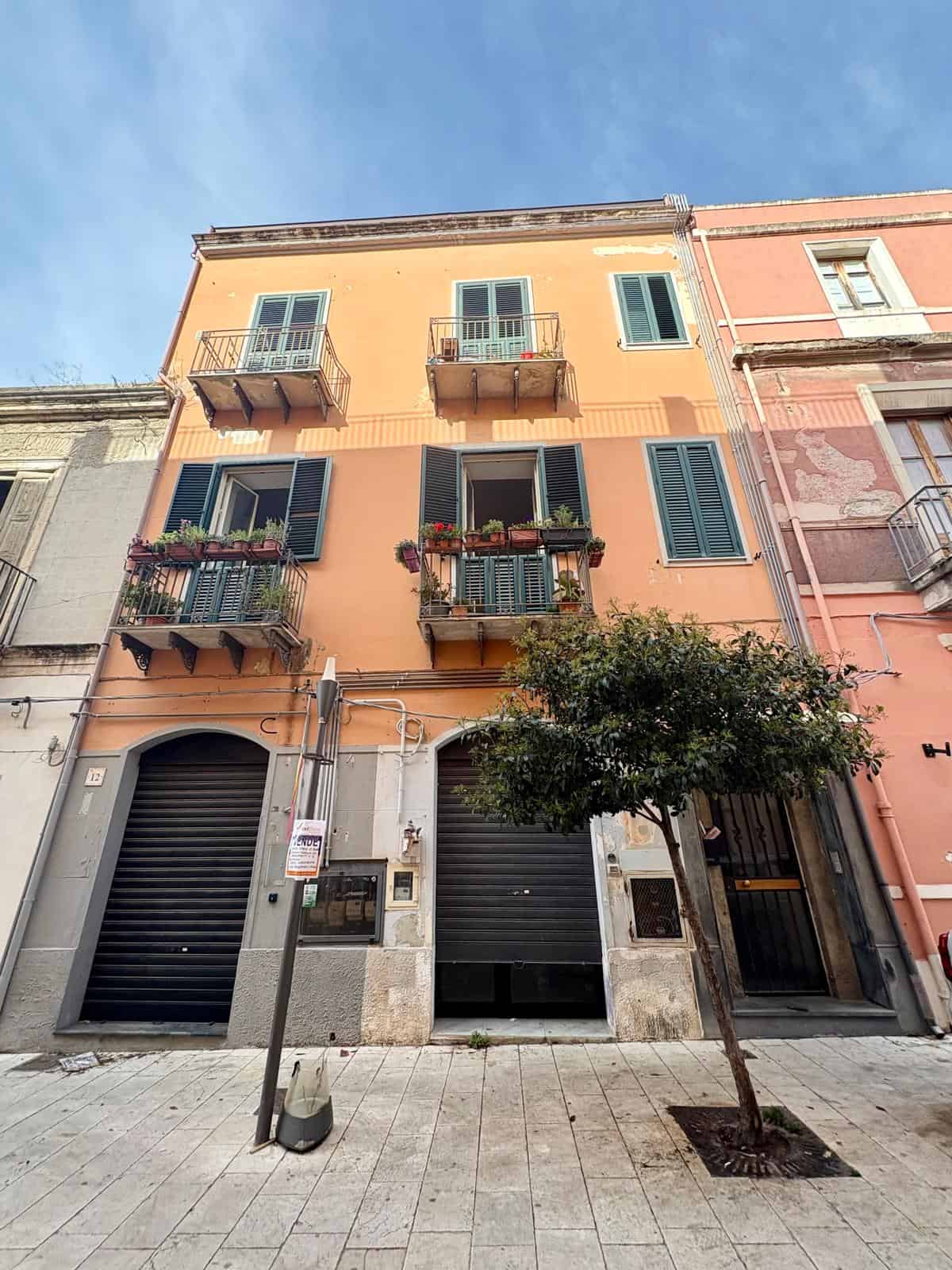 Vicolo con edificio residenziale di charme, caratteristiche balconate con piante, finestre con persiane verdi, atmosfera autentica e accogliente.