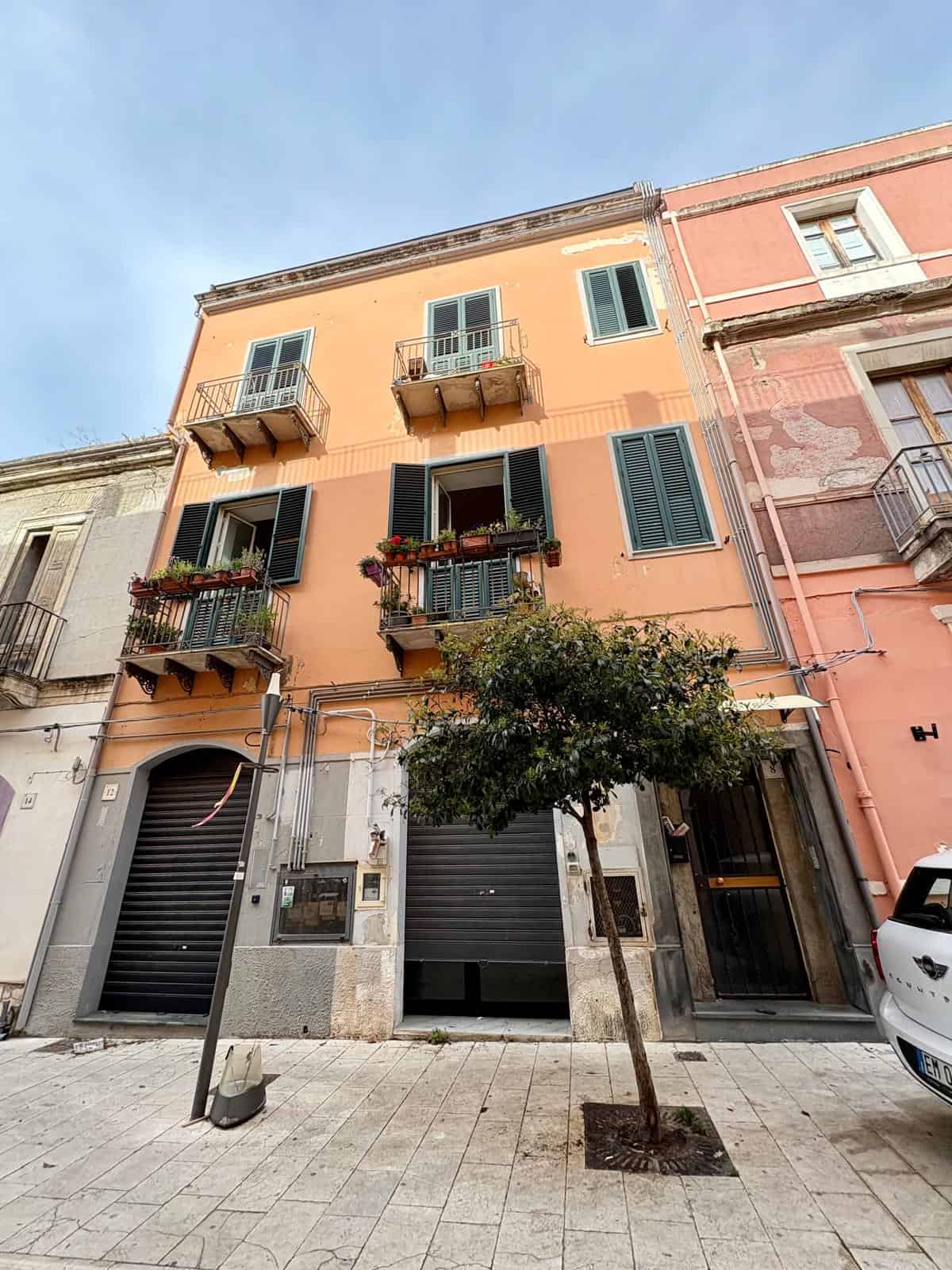 Finestra e balcone di un edificio residenziale di colore arancione in stile italiano. Scene di vita urbana con facciata decorata e piccolo albero sulla strada.