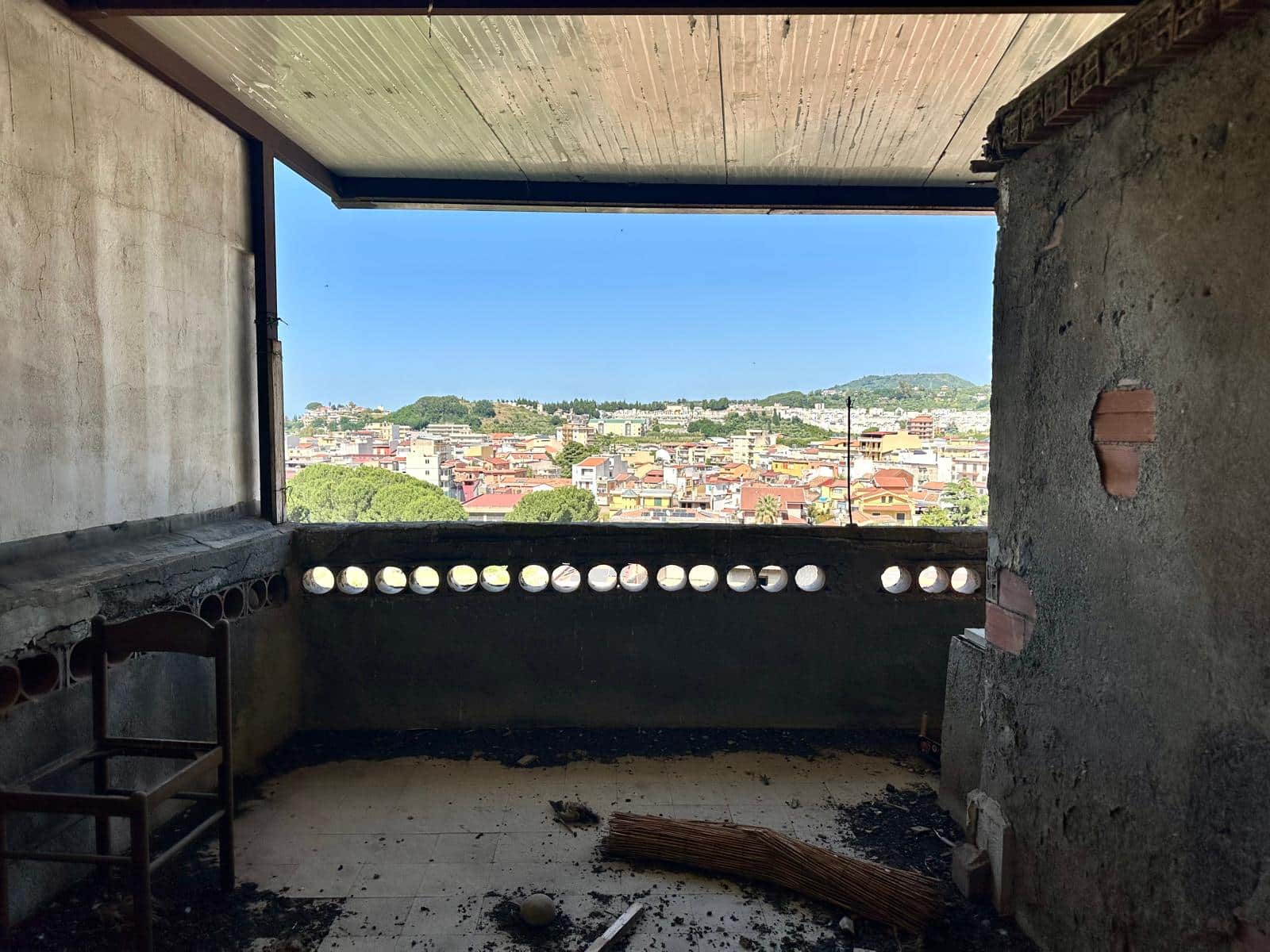 Balcone di un appartamento in fase di ristrutturazione con vista panoramica sulla città e le colline, ambiente in costruzione con elementi di edilizia grezza e arredi minimalisti.