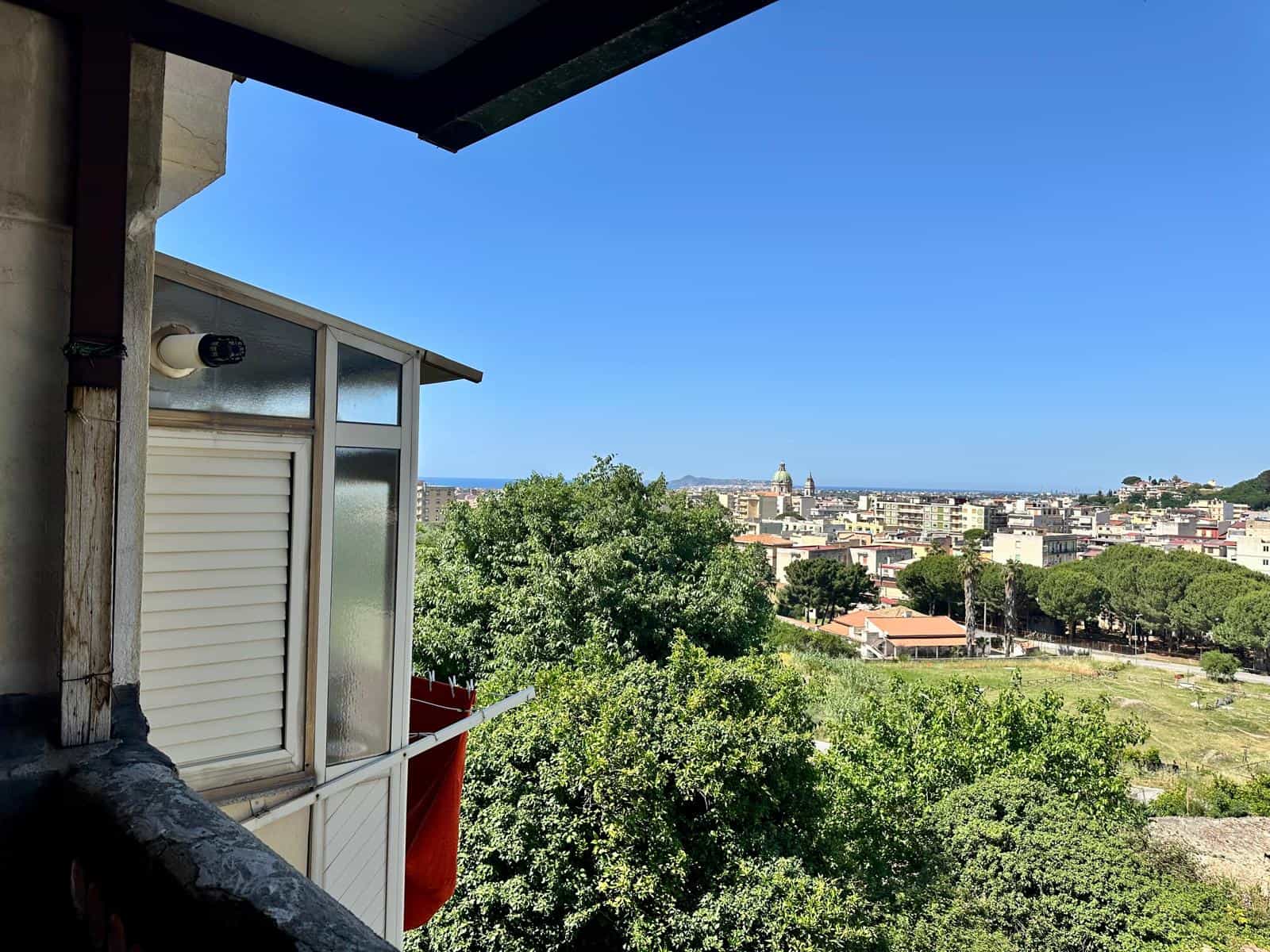 Balcone con vista sulla città e il mare, appartamento in affitto a NextCasa, Sicilia, vista panoramica, ambiente luminoso, zona residenziale con spazi verdi.